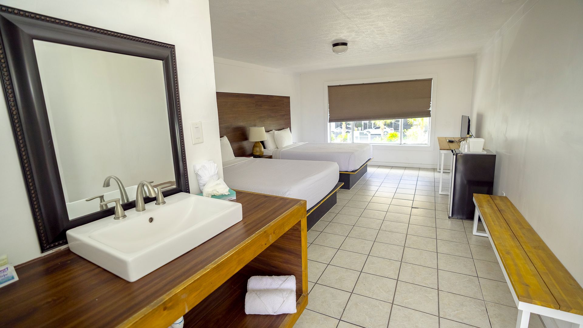 A hotel room with two beds , a sink and a mirror.