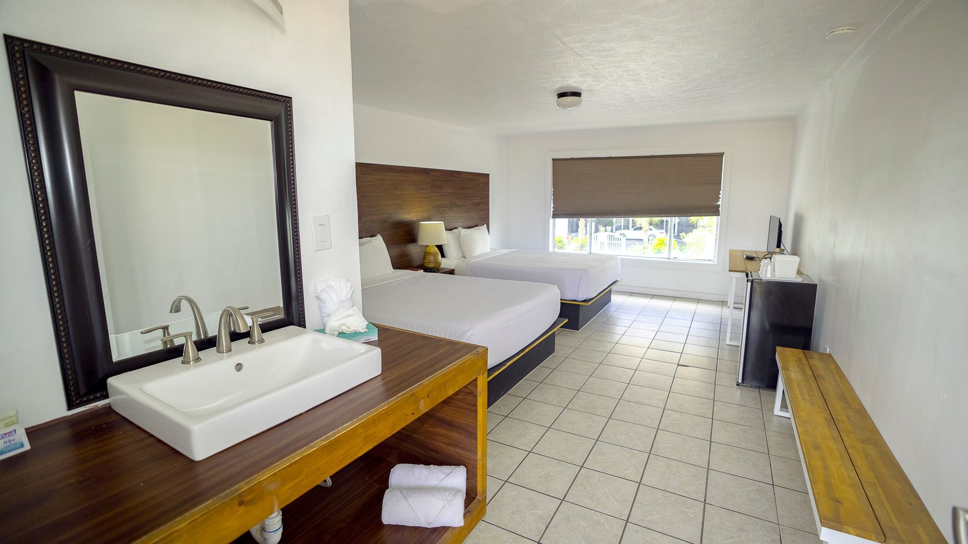 A hotel room with two beds , a sink and a mirror.
