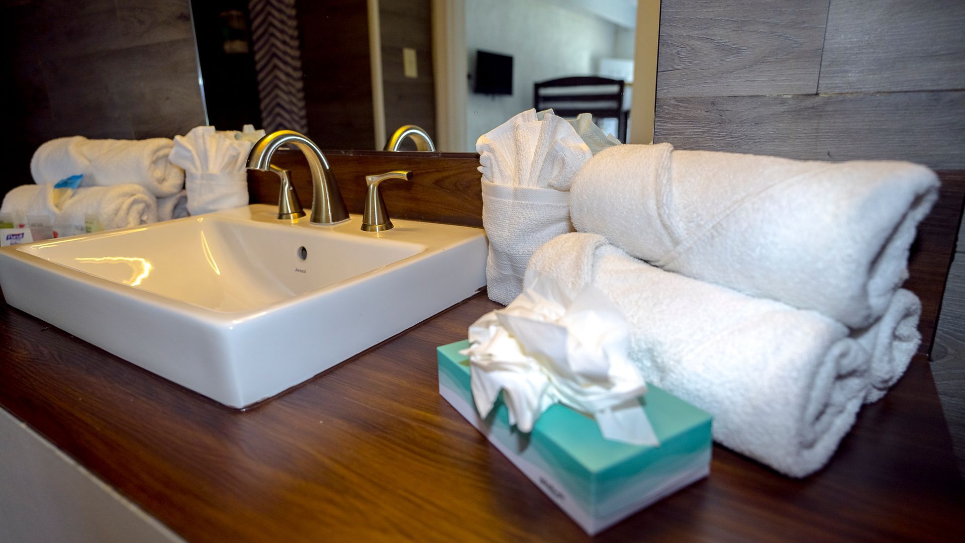 A bathroom with a sink , tissues , and towels on the counter.