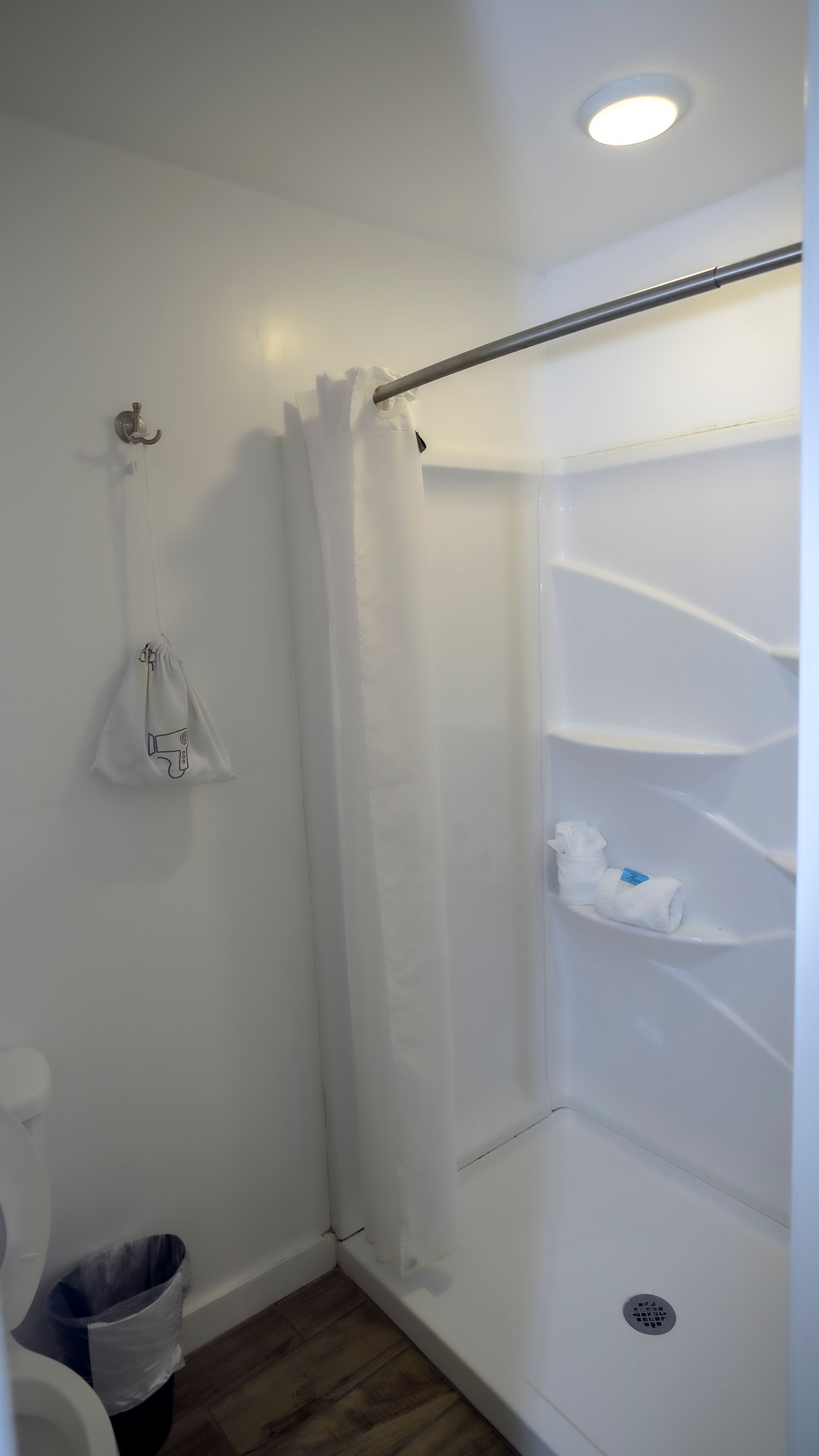 A bathroom with a shower and a trash can.