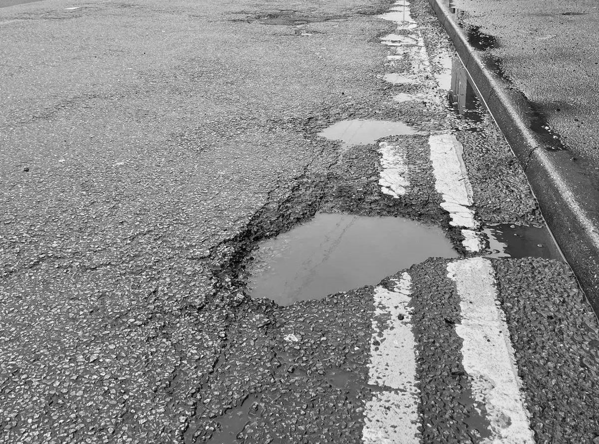 Potholes filled with water on a cracked asphalt road with white lane lines.