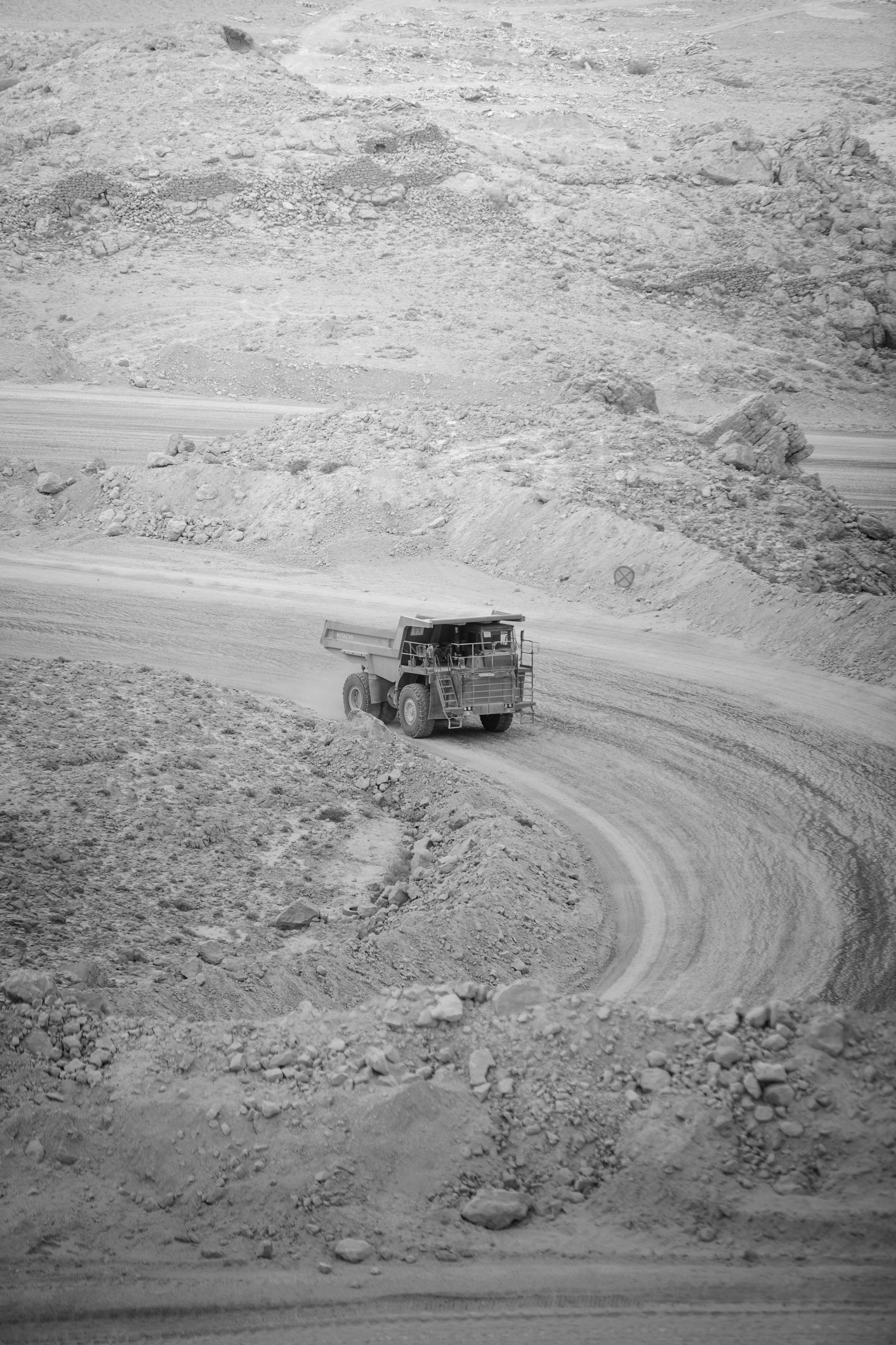 Motorcyclist riding towards a dark tunnel entrance on a dirt road, flanked by rock walls.