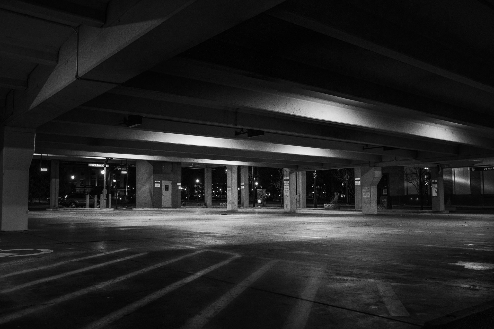Underneath a structure, shadows and light cast across a large open space with support pillars.