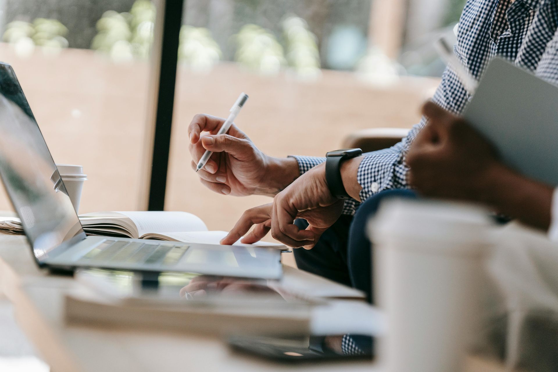 Two people at a table reviewing laptop and notes, one pointing with a pen.