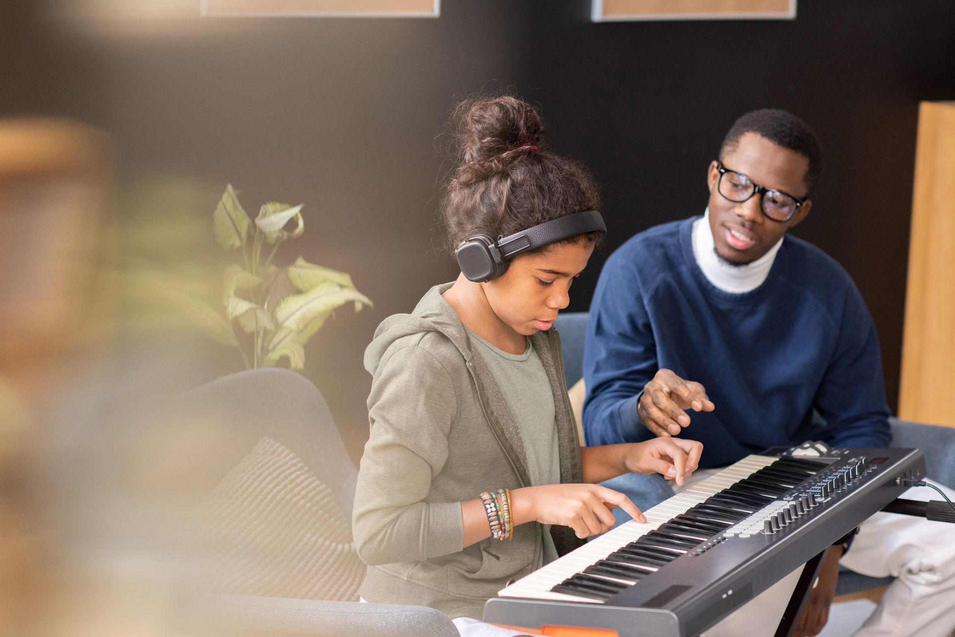Man teaching a girl how to play a keyboard indoors. Both are focused.