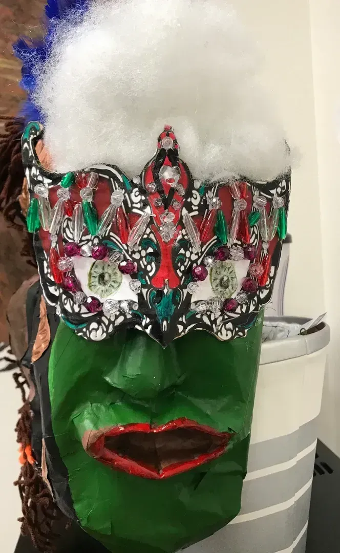 Green mask with jeweled eye covering, white fluff on top, and red lips.