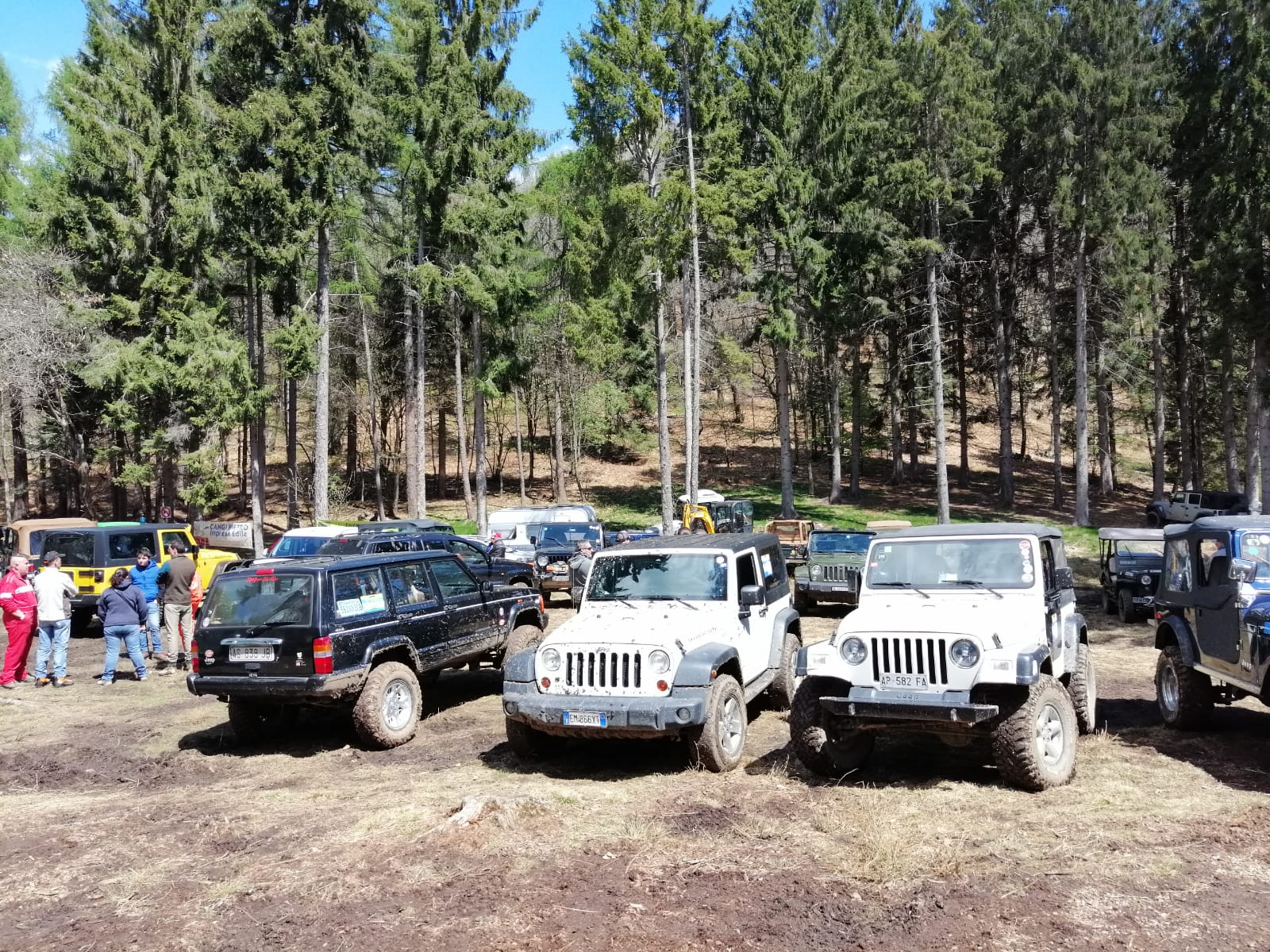 Jeep radunate in una radura fangosa in una foresta, con persone visibili.