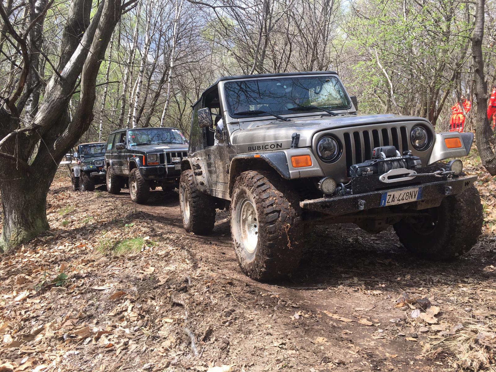 Jeep fuoristrada su un sentiero fangoso in una foresta. Una Jeep in primo piano, seguita da altre.