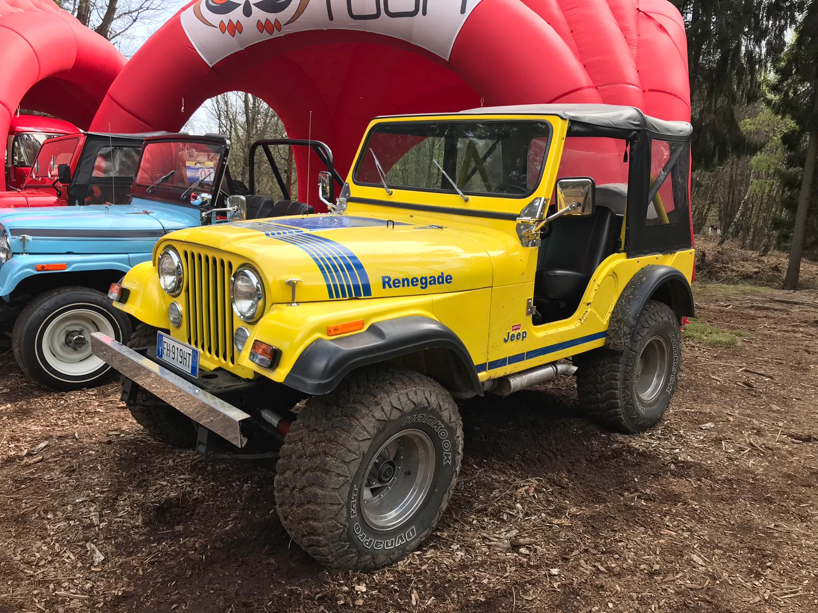 Veicolo fuoristrada Jeep Renegade giallo con strisce da corsa blu, parcheggiato vicino a un arco gonfiabile rosso.