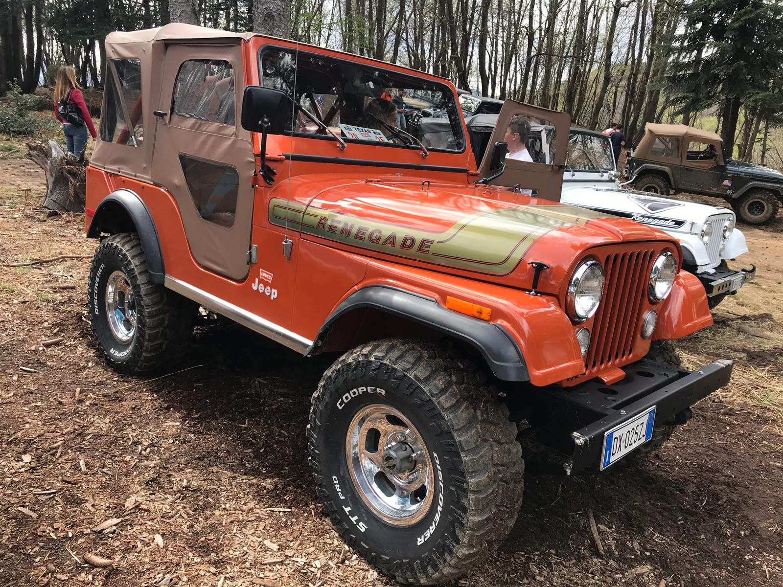Jeep Renegade arancione parcheggiata all'aperto su uno sterrato. Capote marrone, paraurti anteriore nero e cerchi cromati.