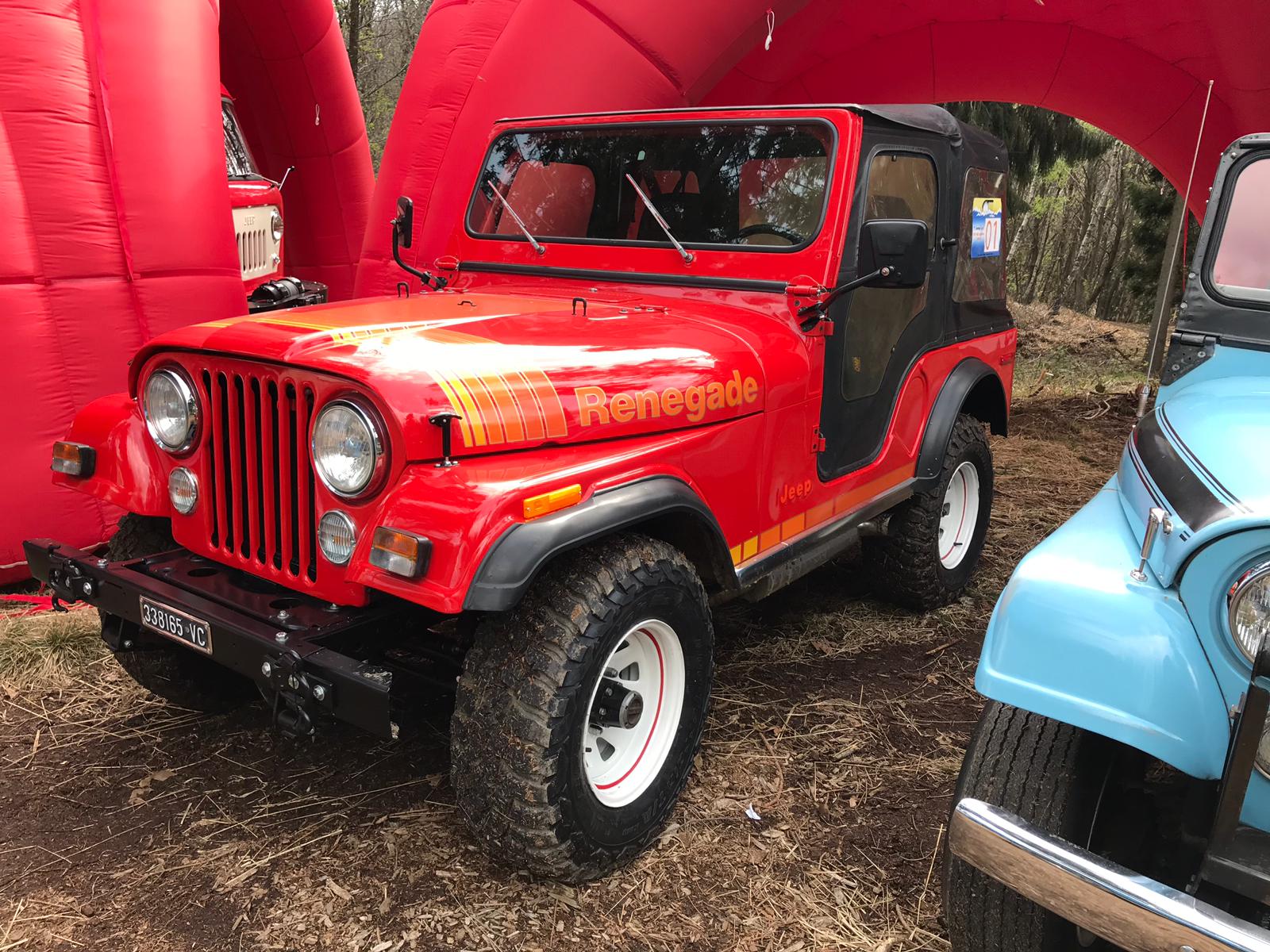 Jeep Renegade rossa con dettagli neri, parcheggiata sotto un arco rosso. Pneumatici con fascia bianca.