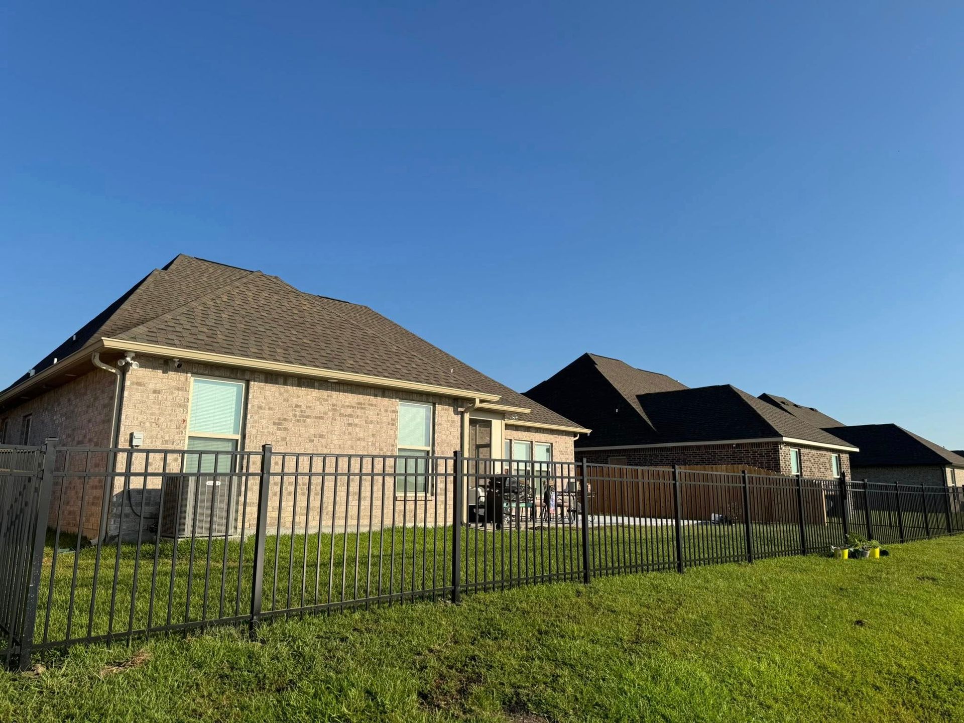 Row of brick houses with dark roofs behind a black metal fence on a sunny day.