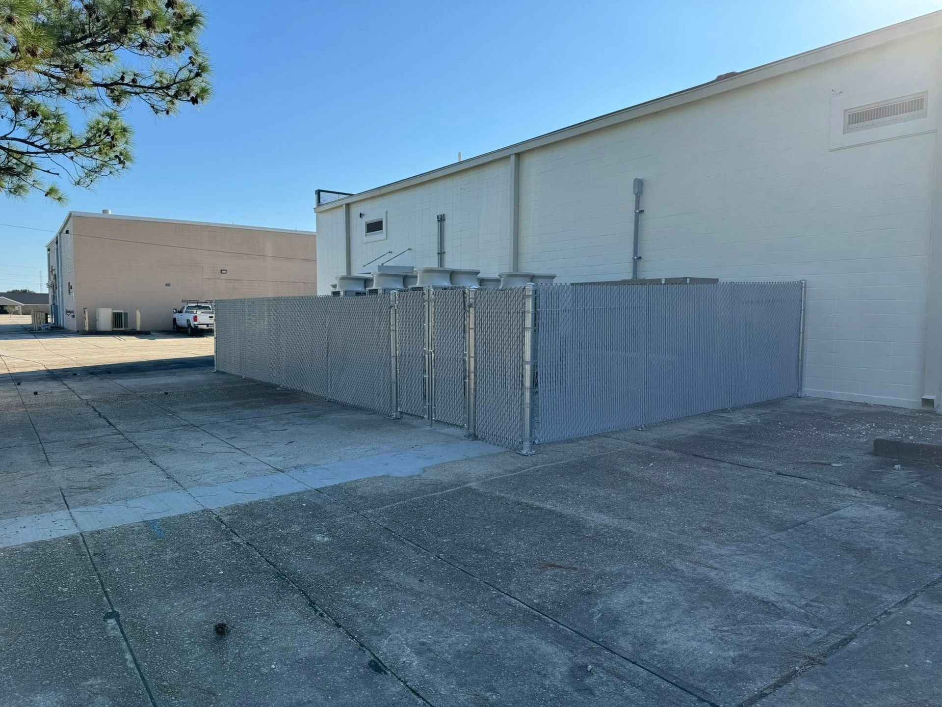 Gray corrugated metal fence in front of a white industrial building on a sunny day.