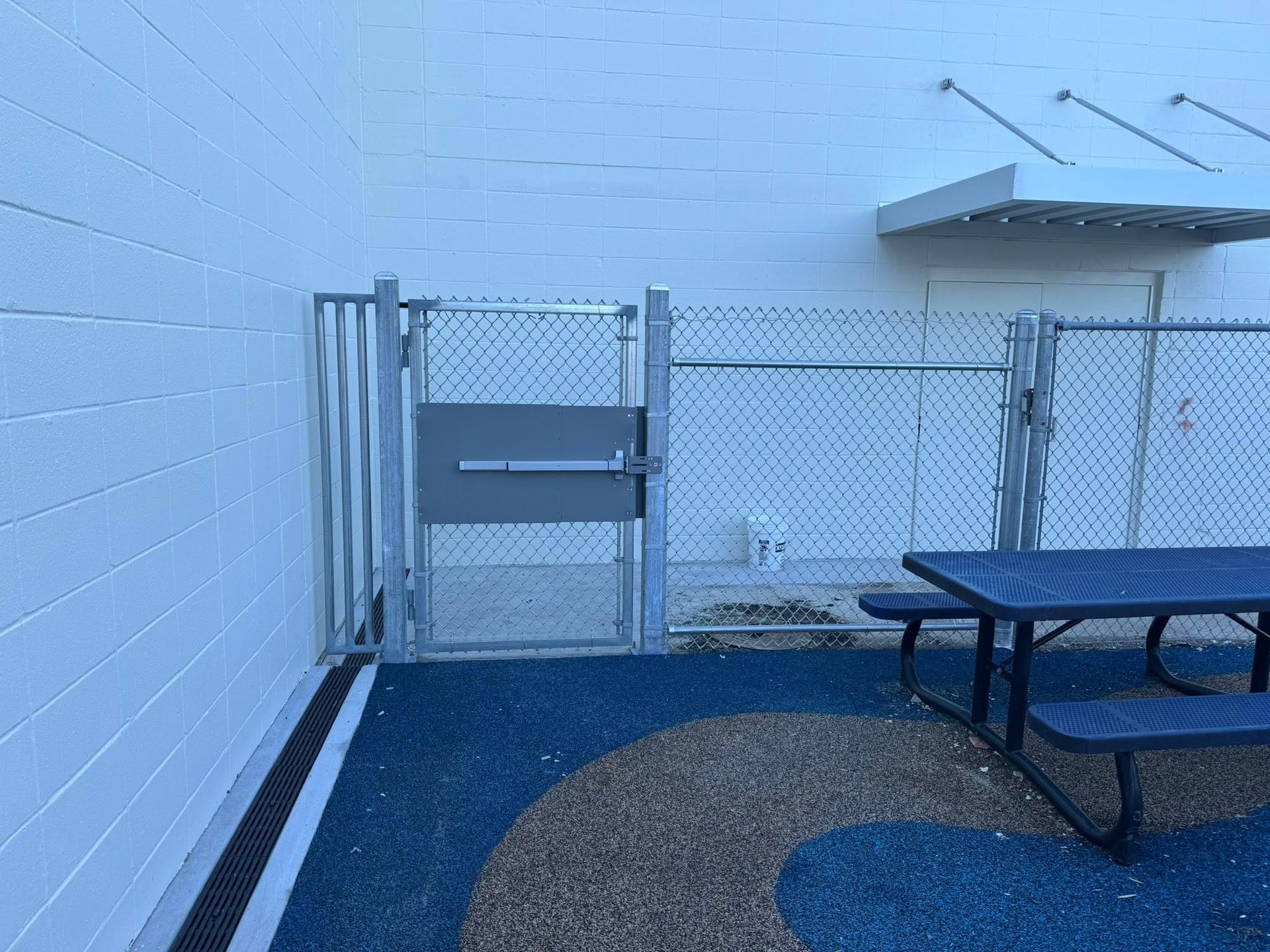 A chain-link fence gate with a metal door attached, leading to an outdoor seating area.