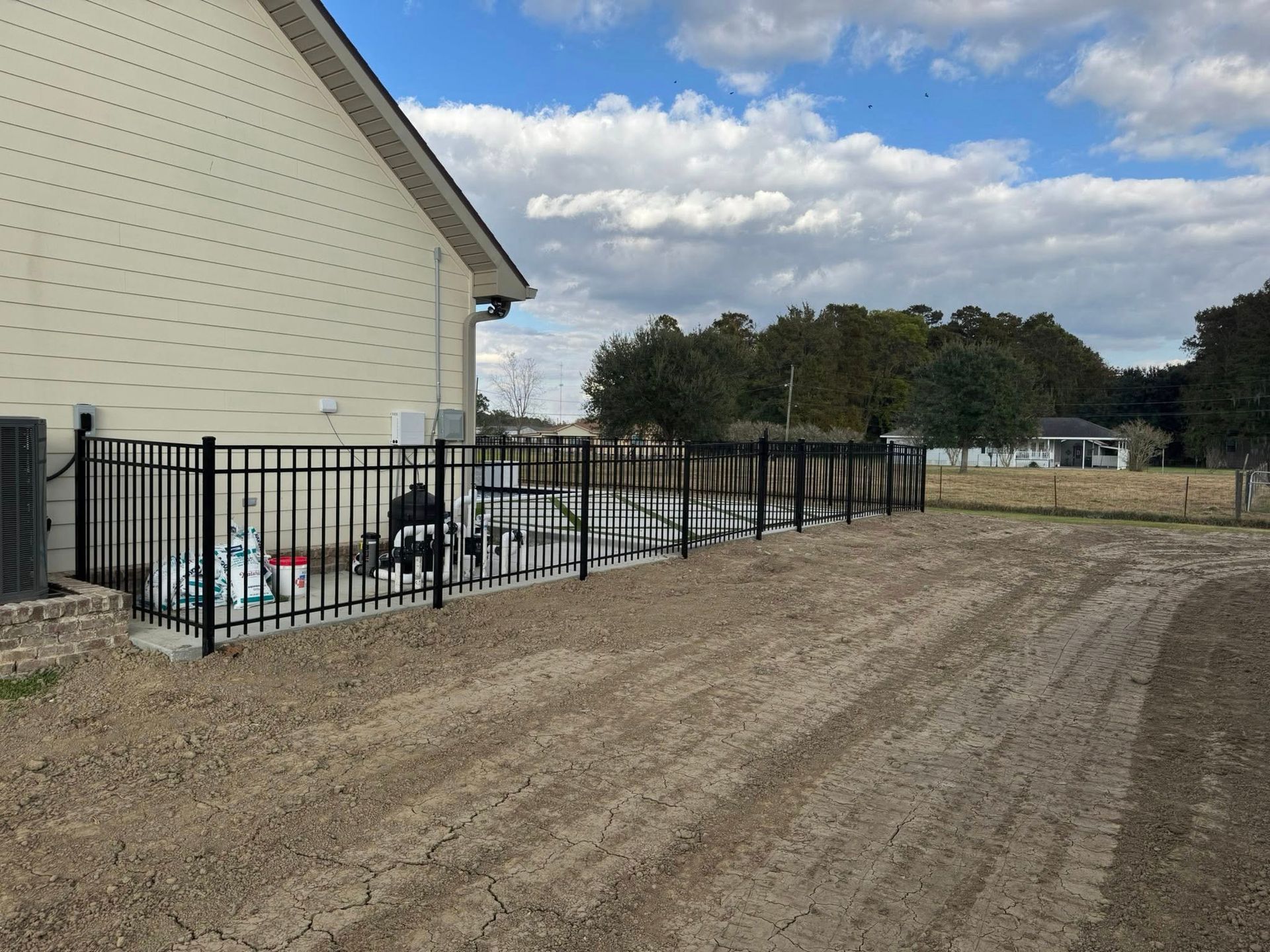 Black metal fence along a gravel area beside a beige house on a cloudy day.