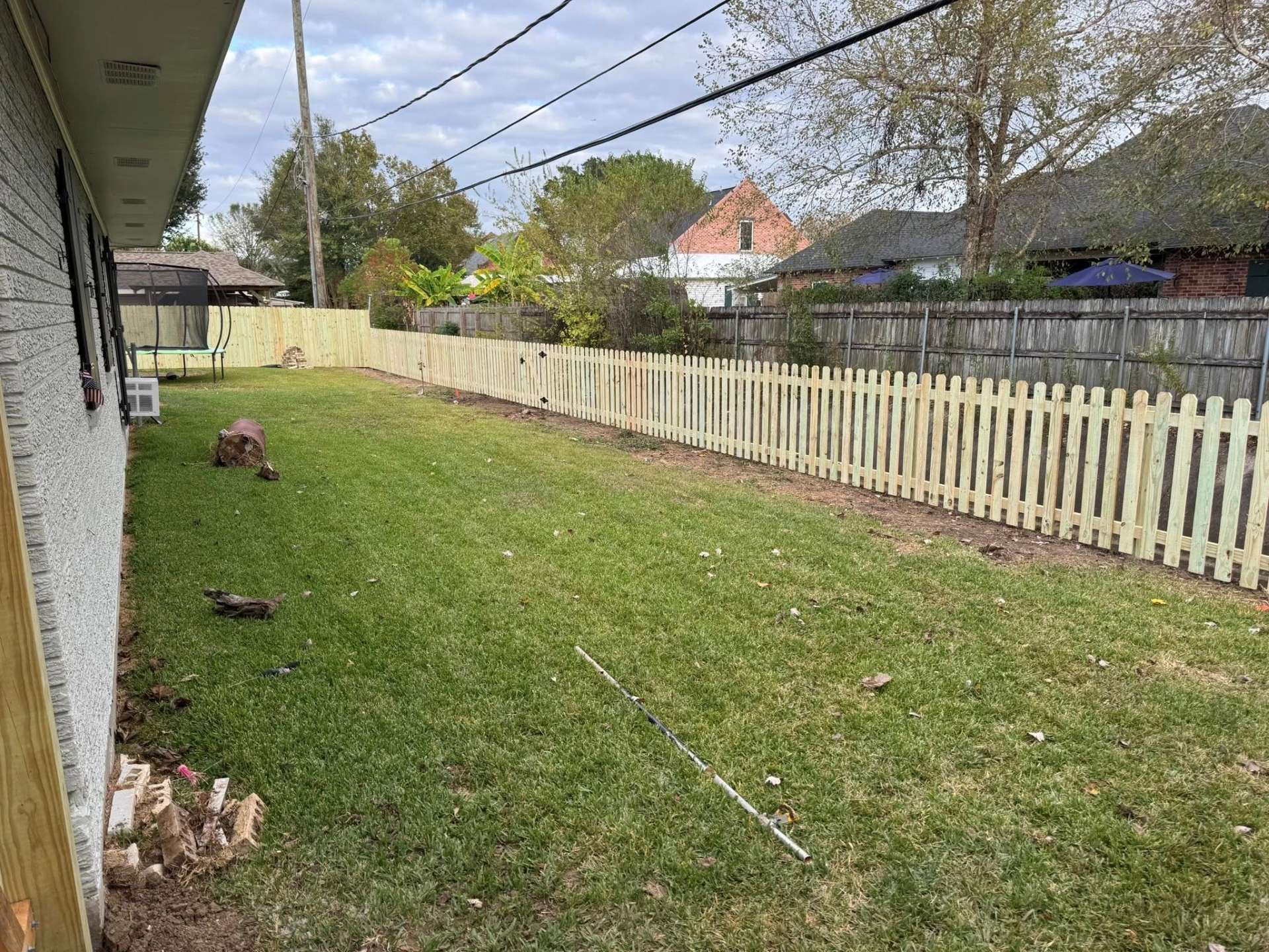 Lawn and picket fence beside a house. Bare tree trunk and utility lines overhead.