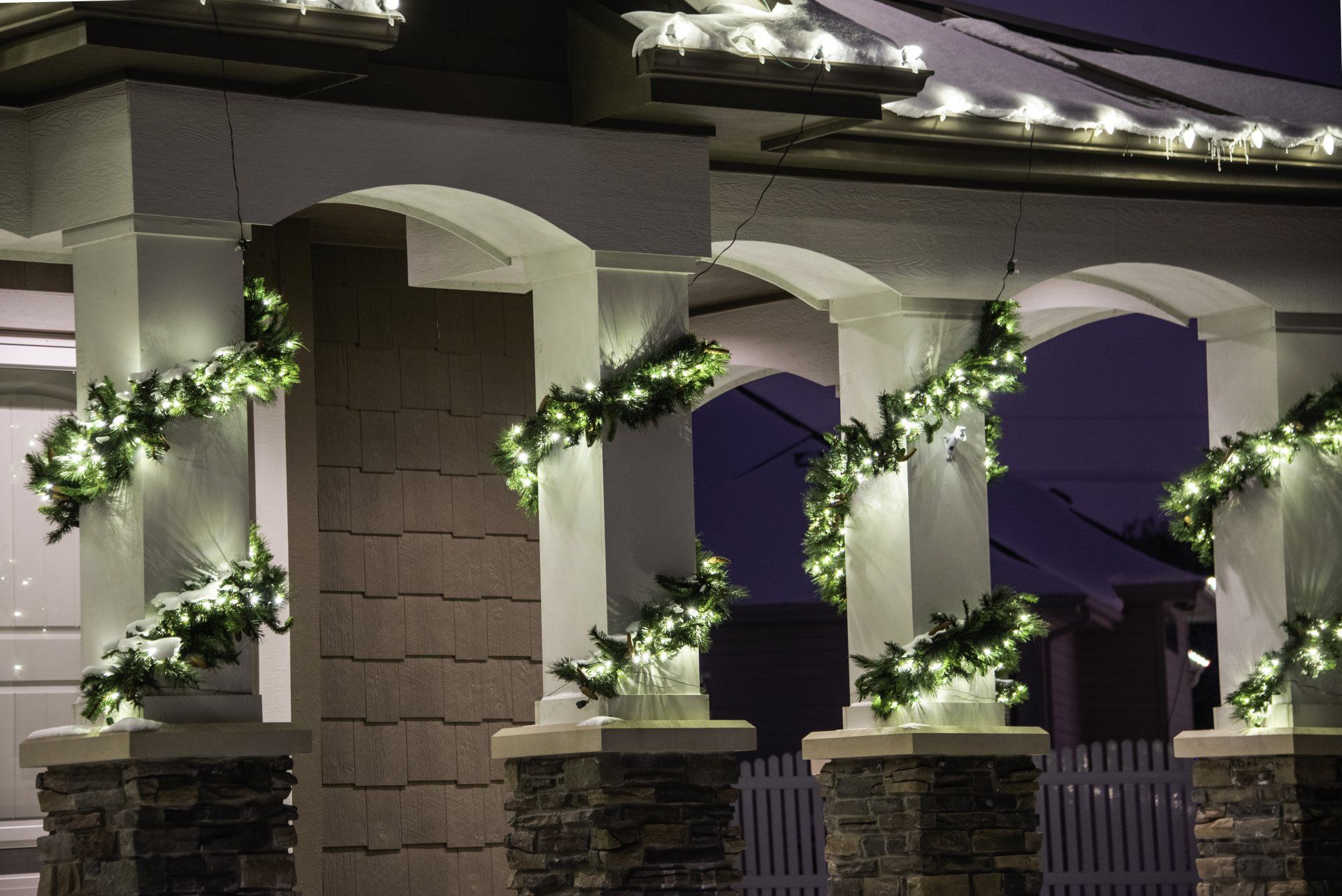 The porch of a house is decorated with christmas lights and garlands.