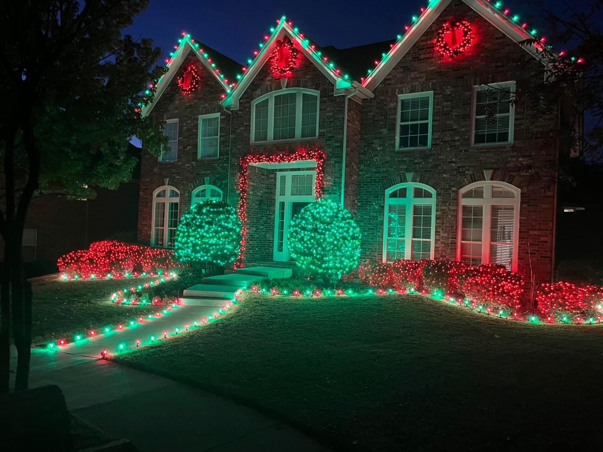 A large brick house decorated with red and green christmas lights