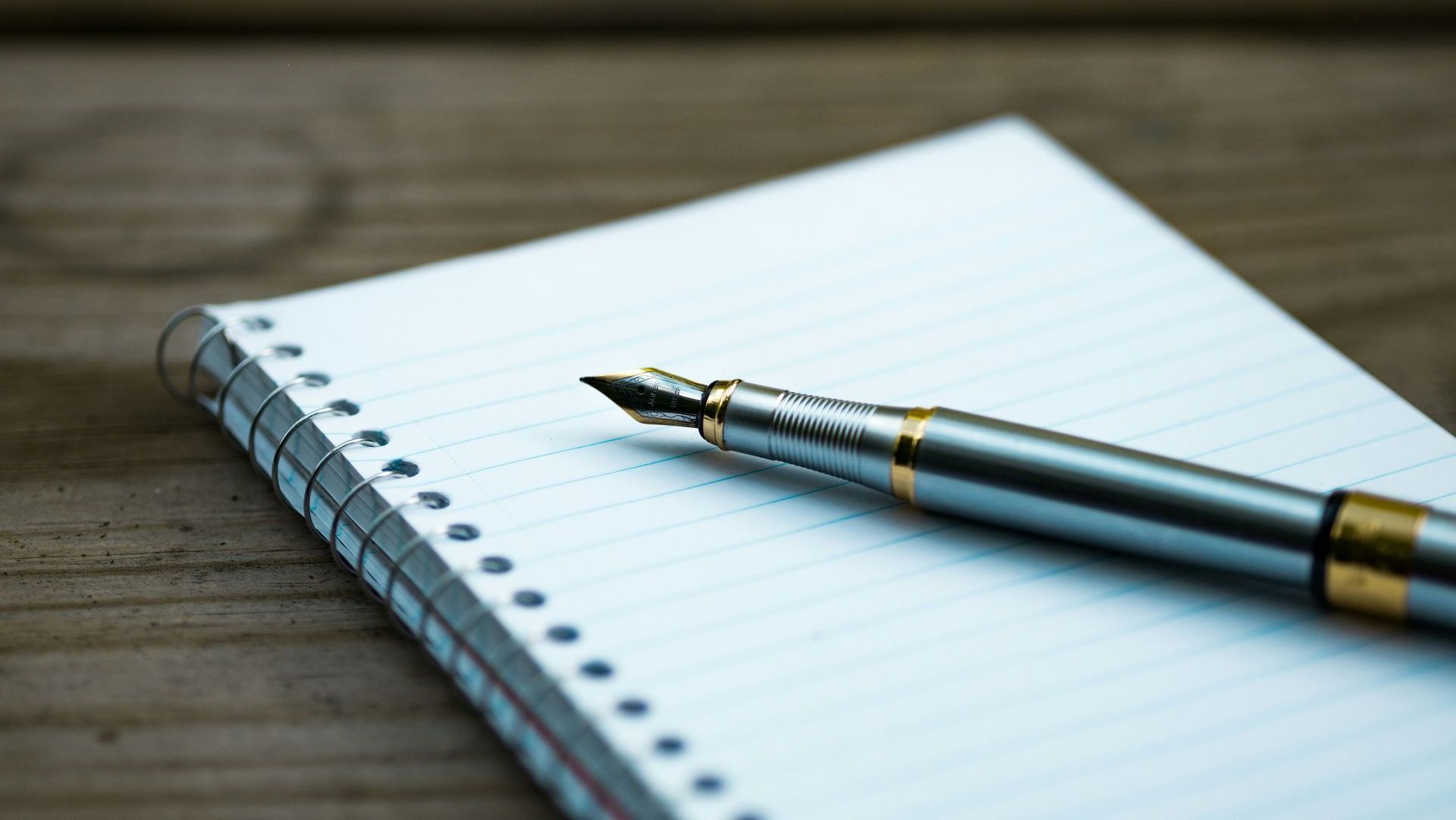 A pen is sitting on top of a notebook on a wooden table.