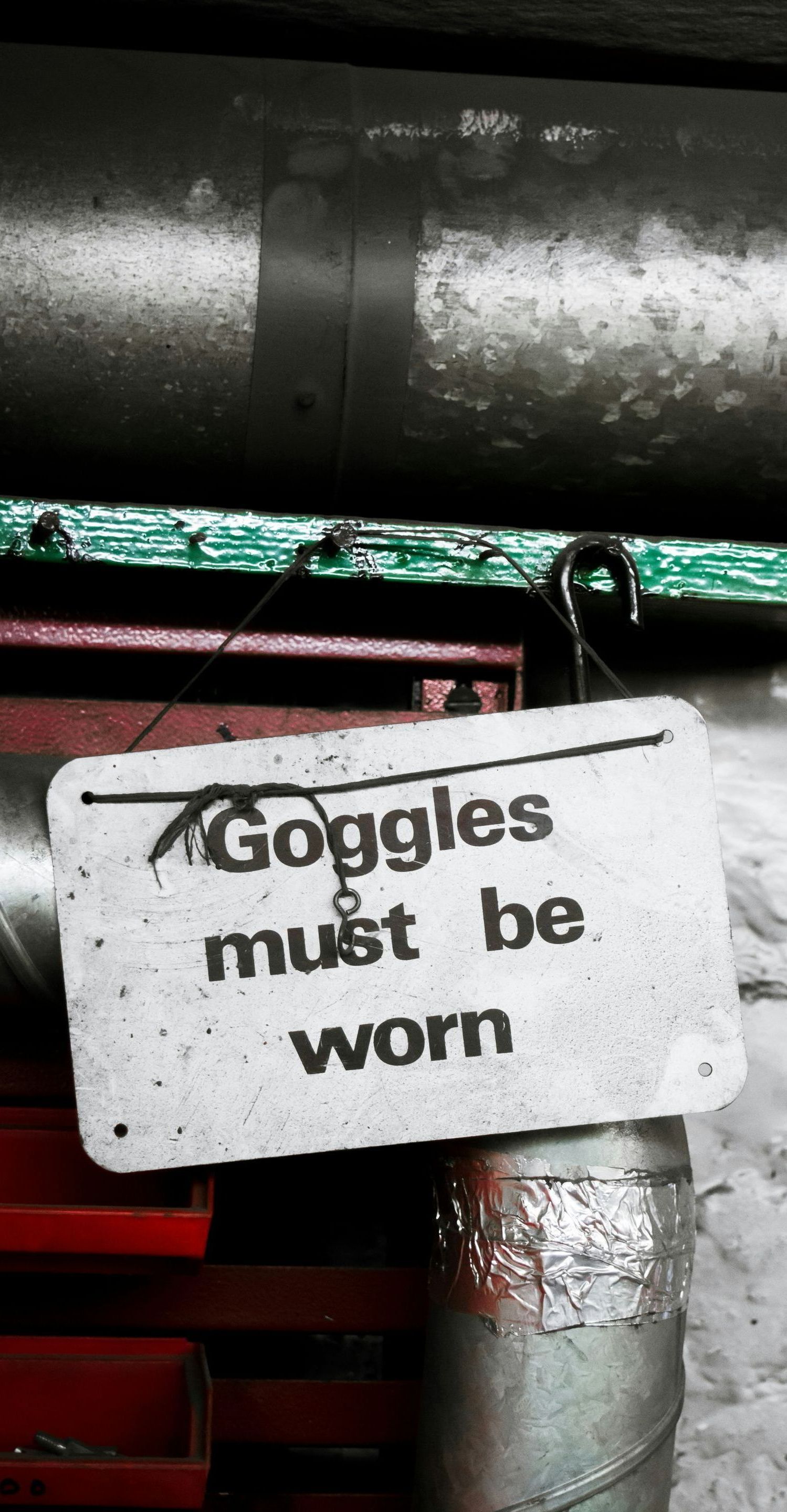 A sign that says goggles must be worn hangs from a metal pipe