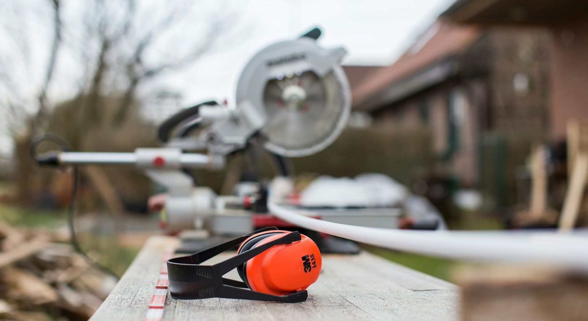 A pair of ear muffs is sitting on a wooden table next to a circular saw.