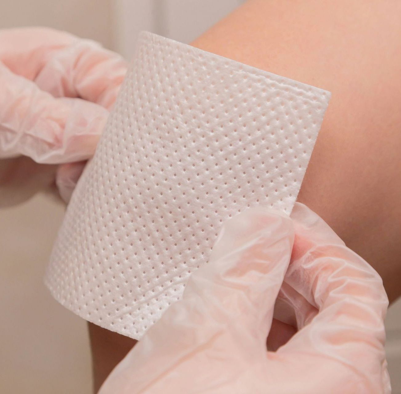 A person wearing gloves is applying a bandage to their knee.