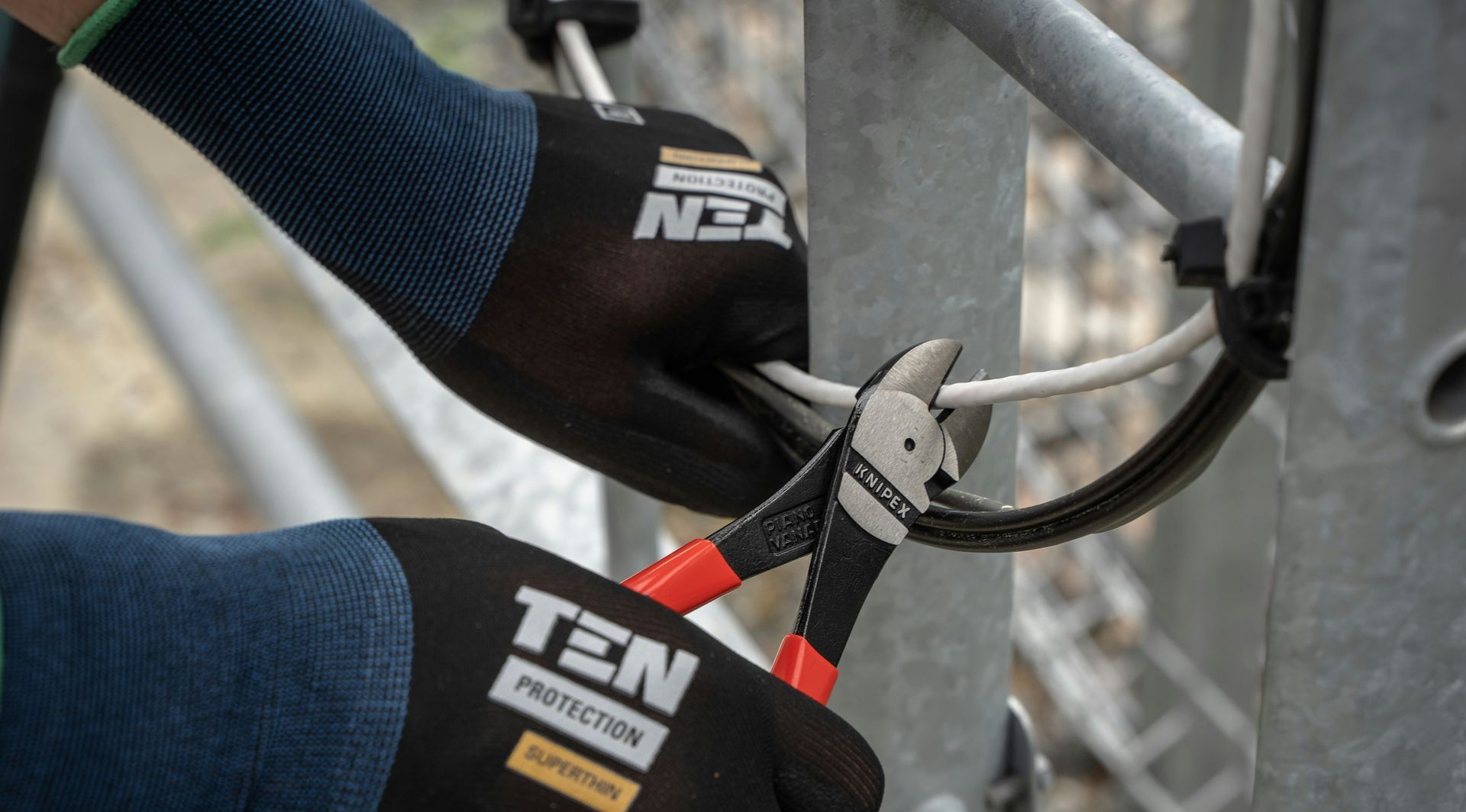 A person wearing gloves is cutting a wire with a pair of pliers.
