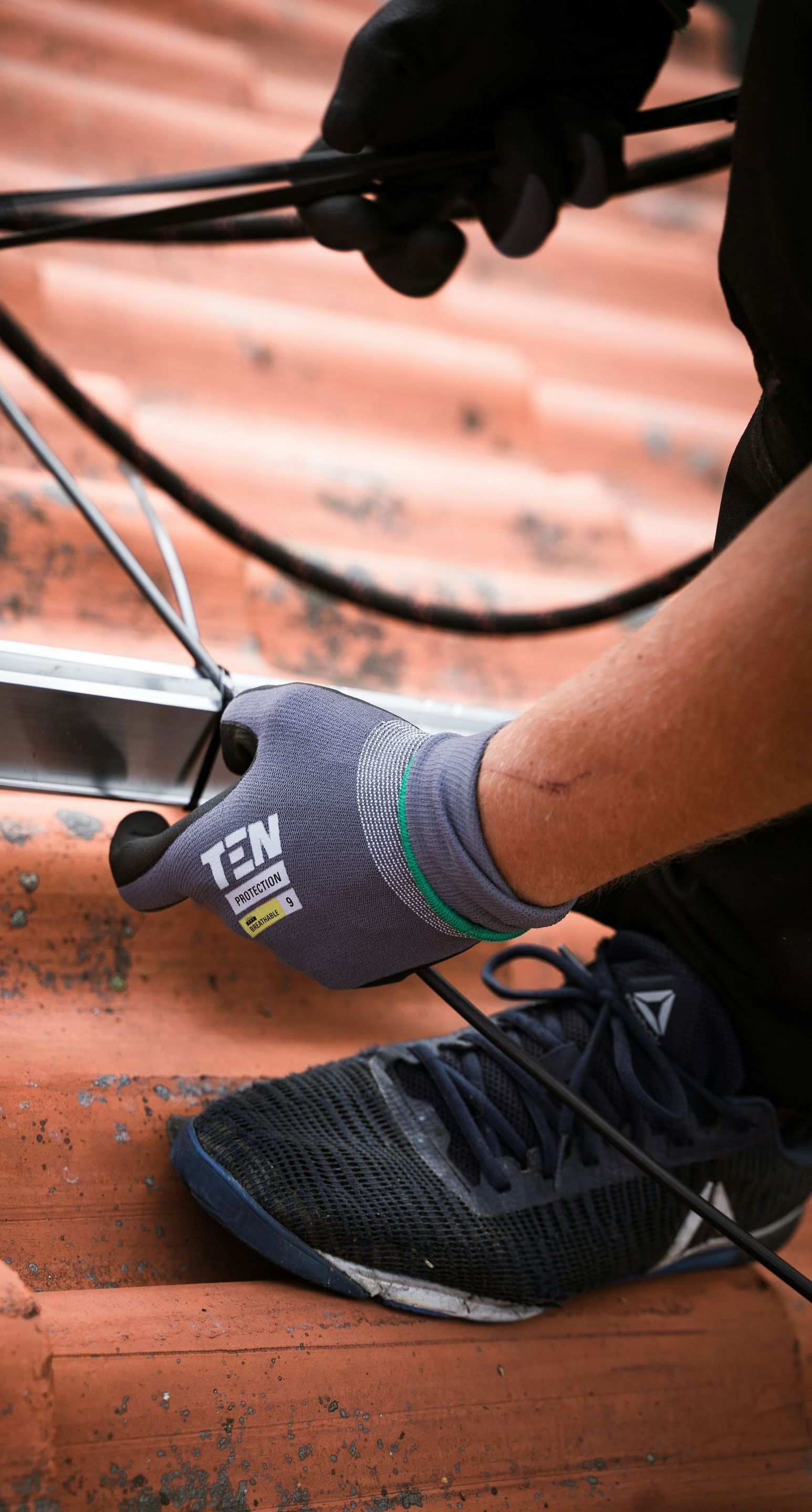 A person wearing gloves is working on a roof with a pair of scissors.