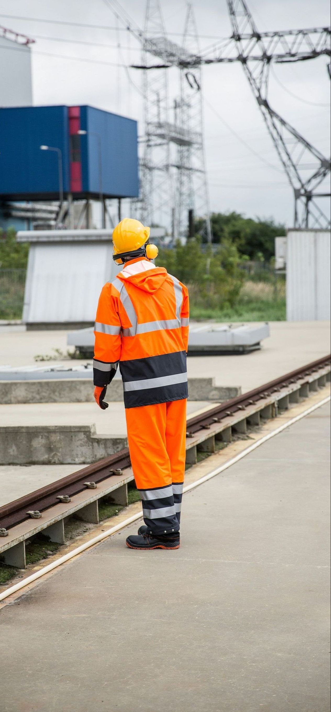 A man in an orange safety suit and hard hat is standing on a train track.
