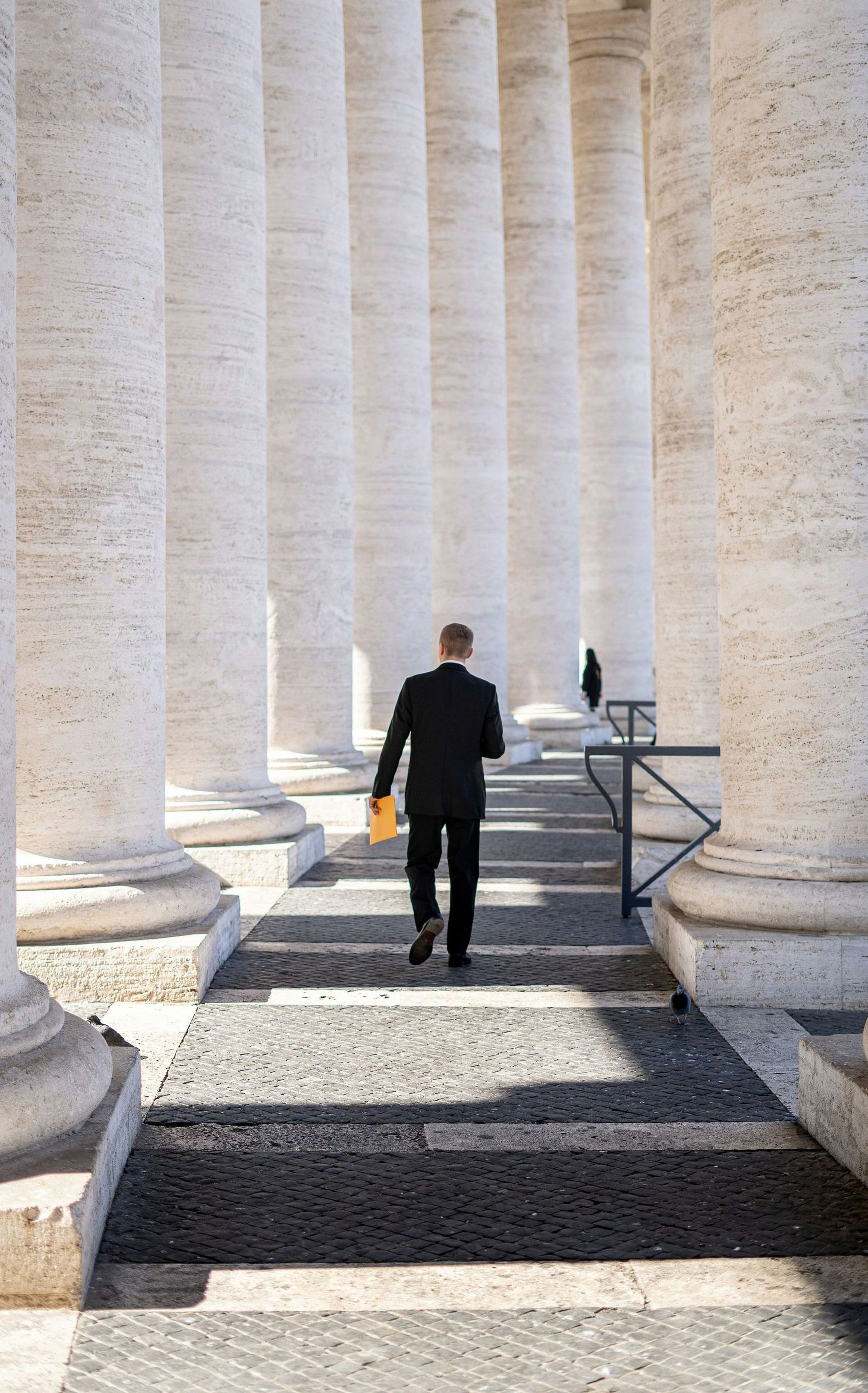 a man in a suit is walking through a row of columns.