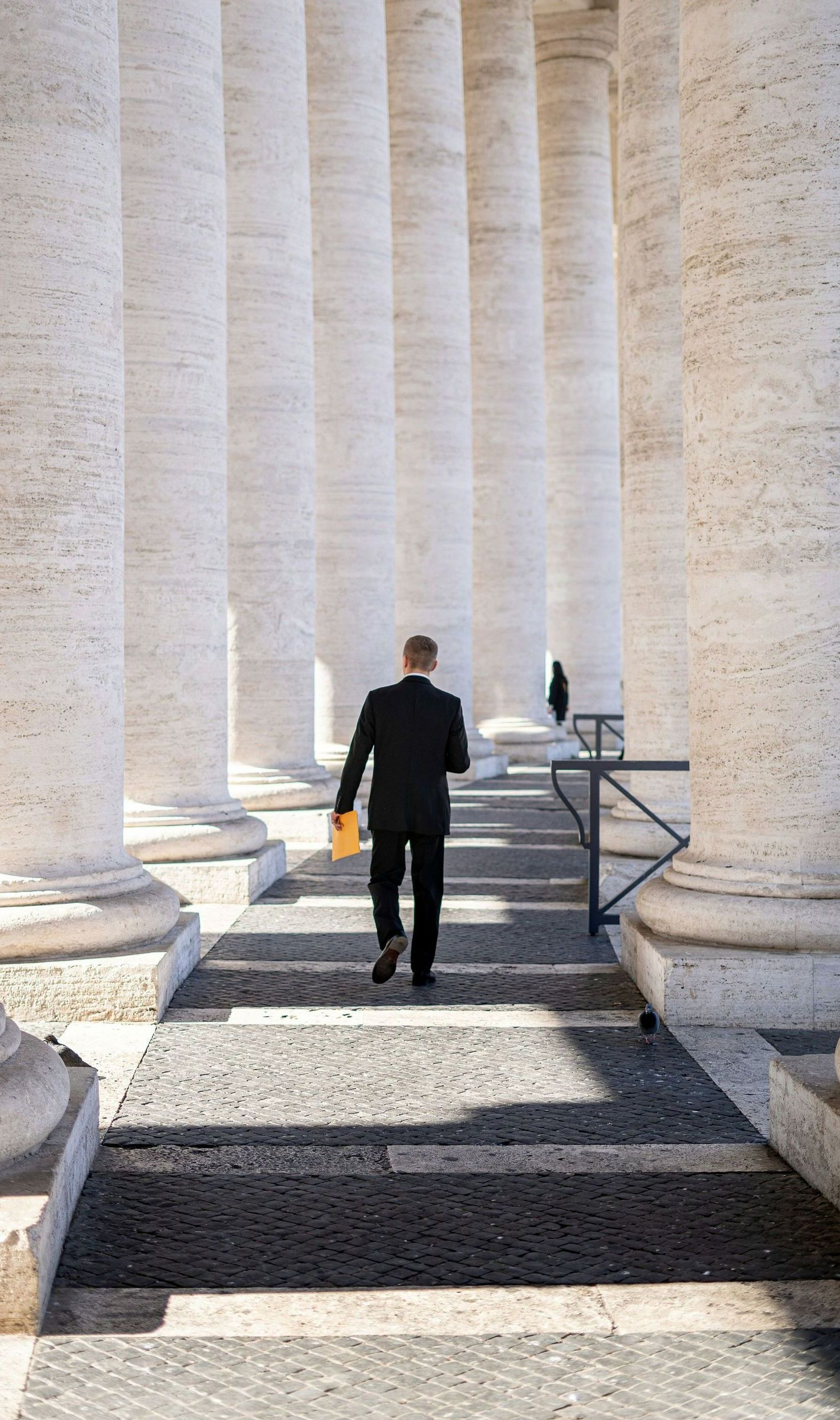 a man in a suit is walking through a row of columns.