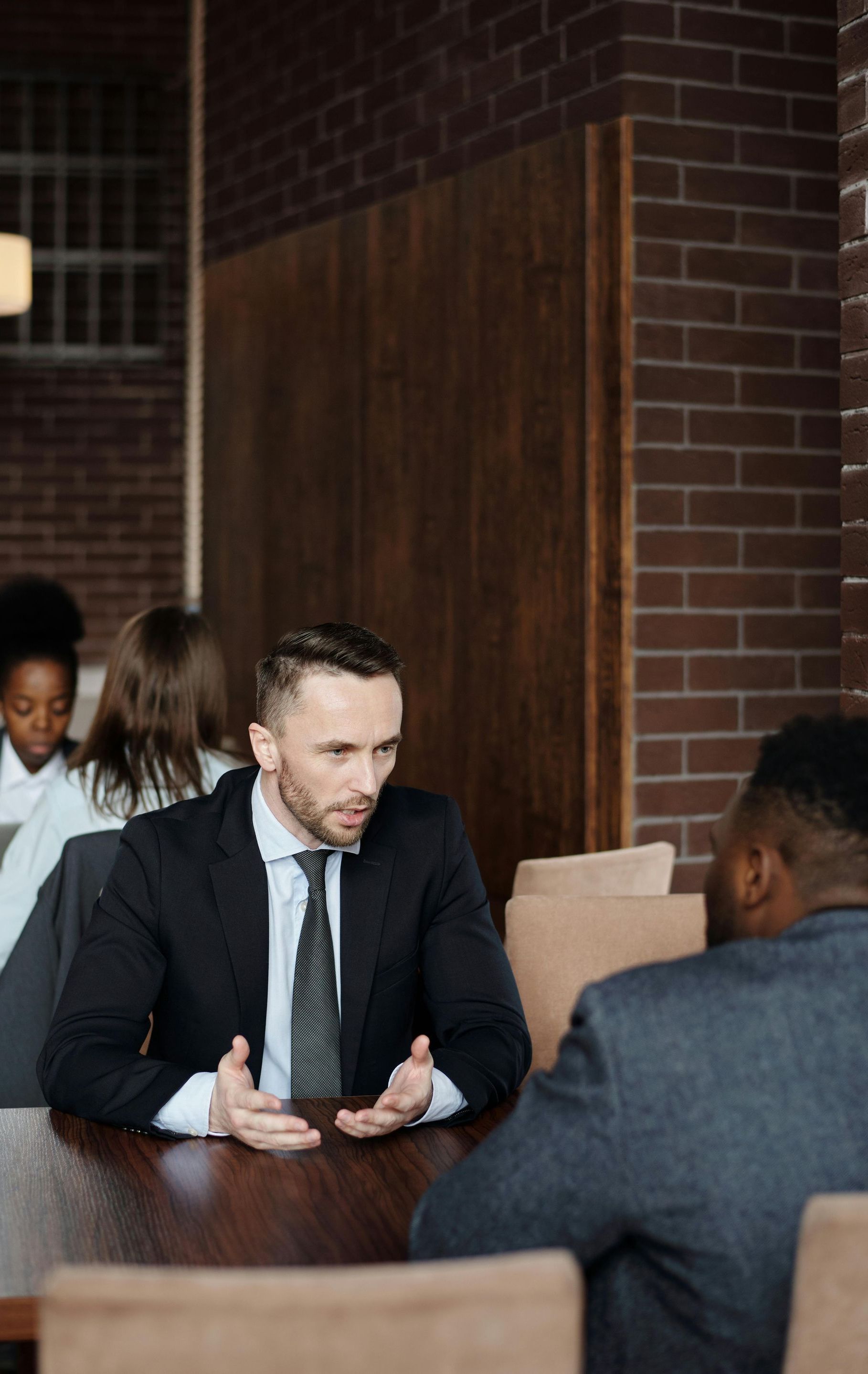 a man in a suit and tie is sitting at a table talking to another man.