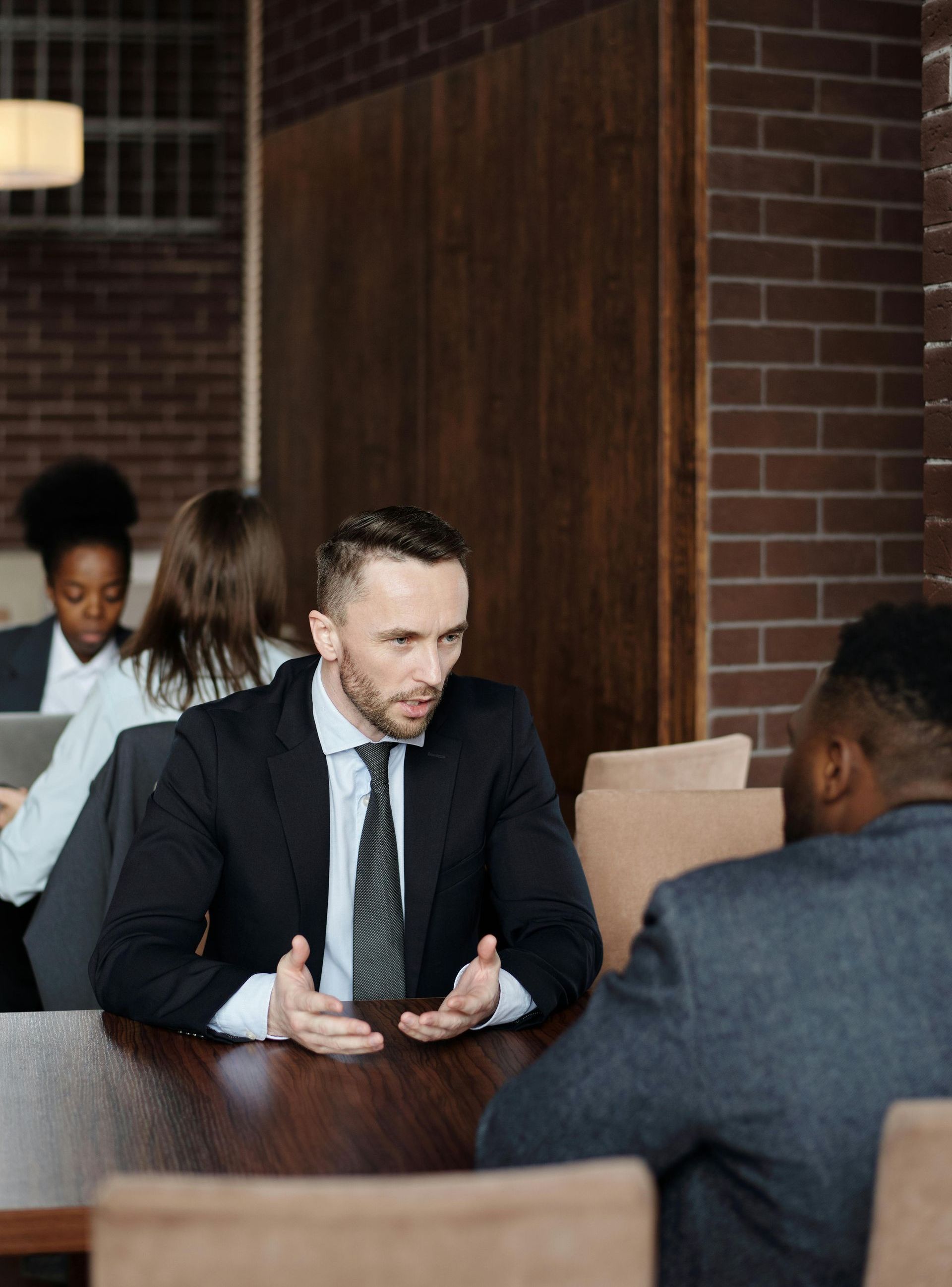A man in a suit and tie is sitting at a table talking to another man.