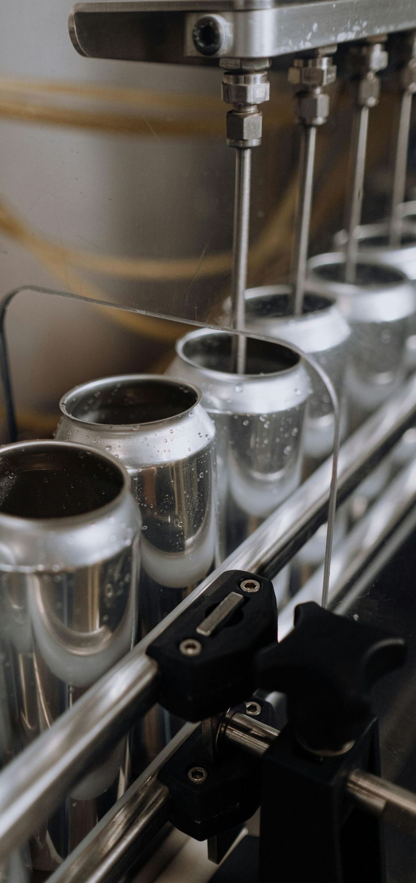 A row of cans are being filled with liquid on a conveyor belt.