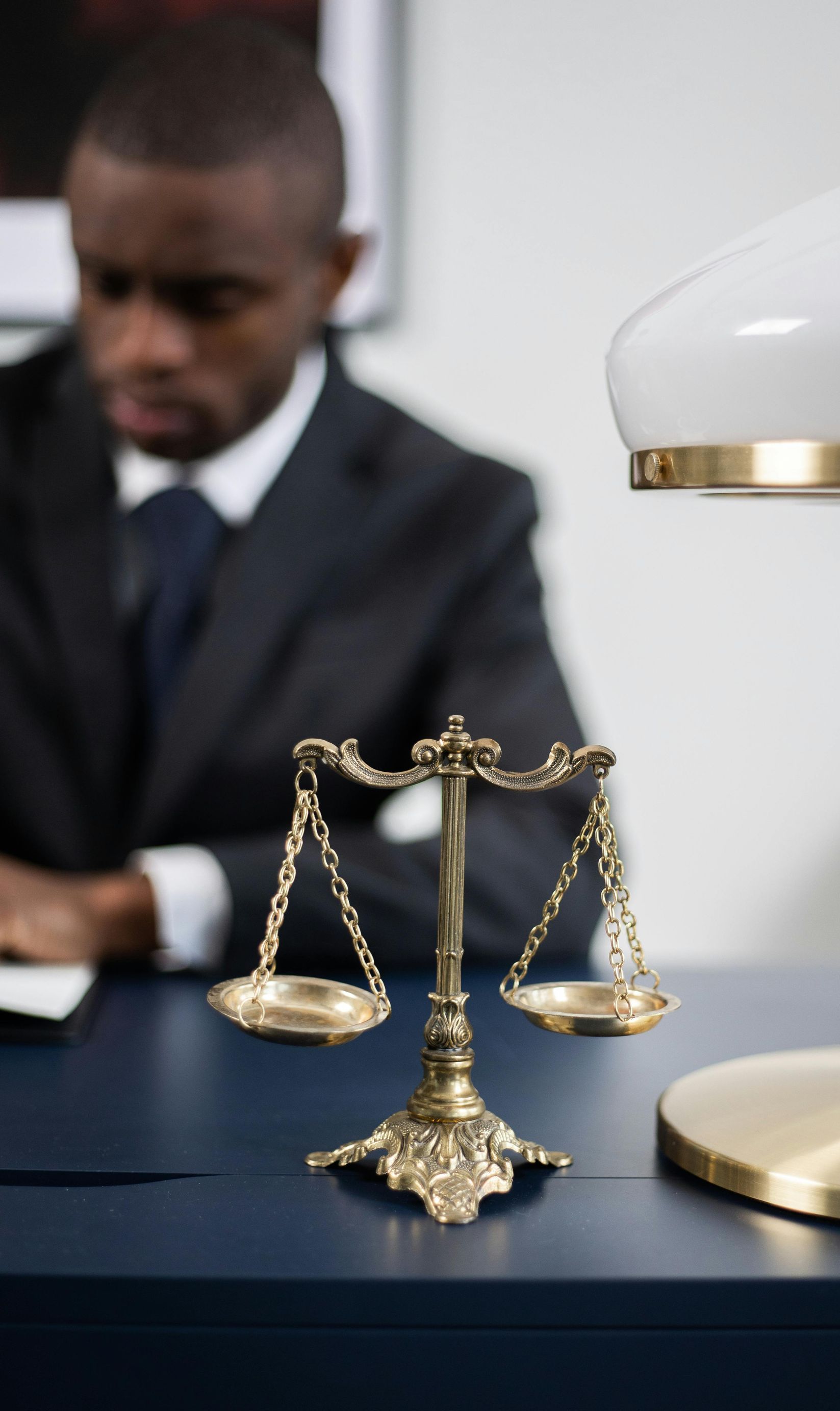 A man in a suit is sitting at a desk with a scale of justice on it.