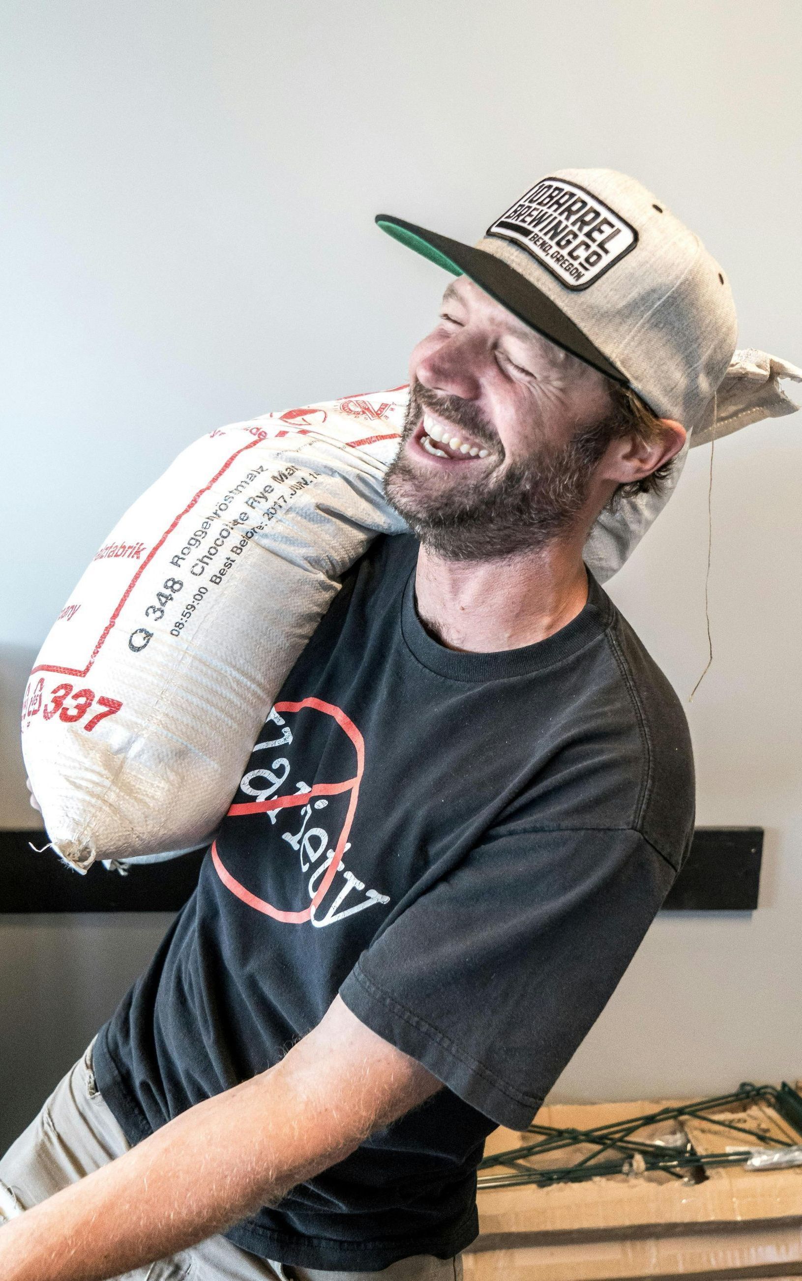 A man wearing a hat is carrying a large bag on his shoulder.