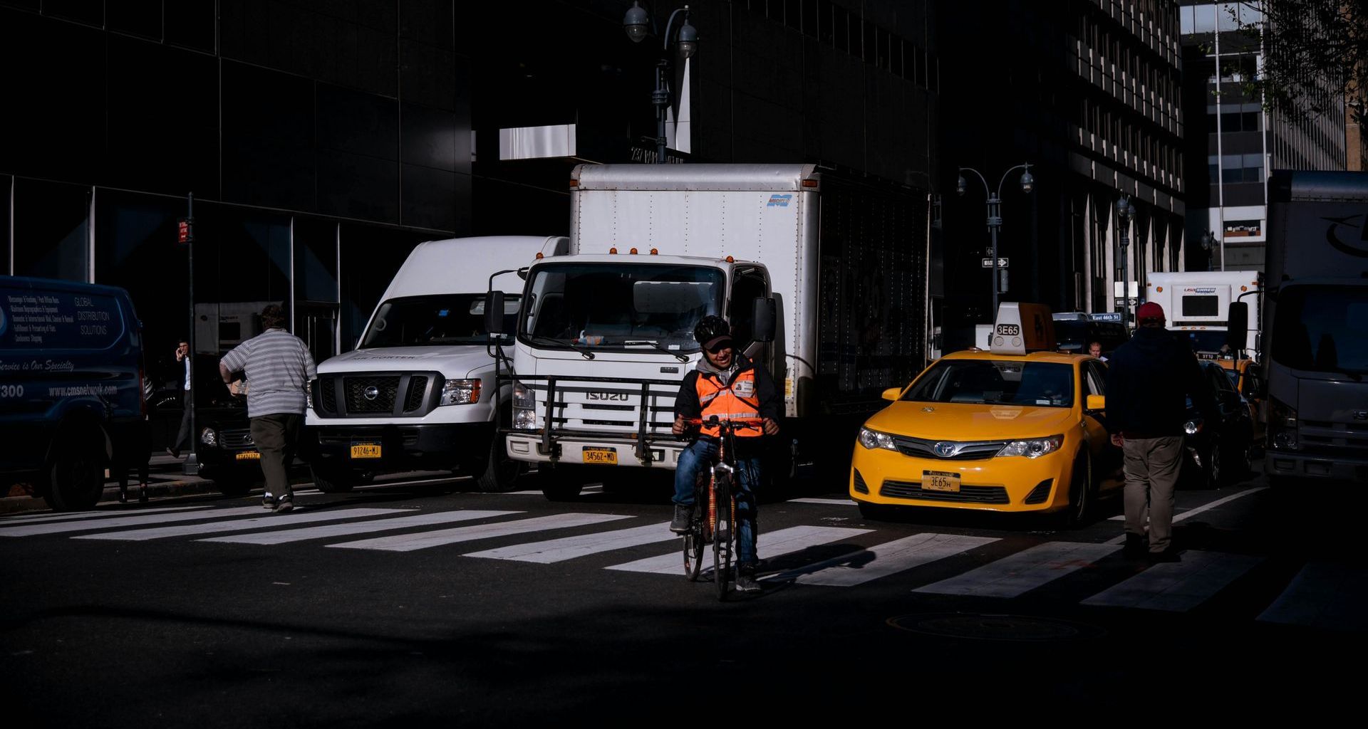 A man is riding a bike on a city street in front of trucks and a car