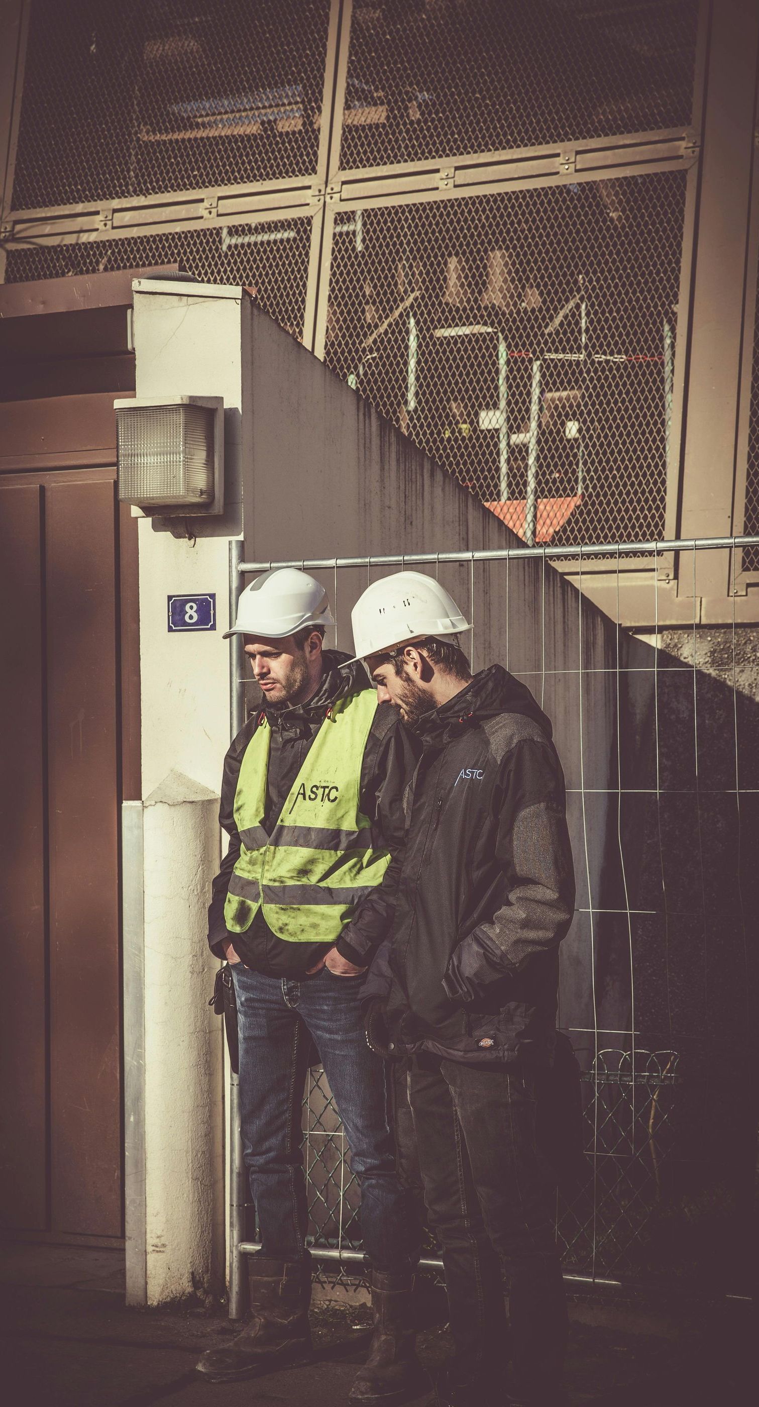 Two men wearing hard hats and safety vests are standing next to each other.