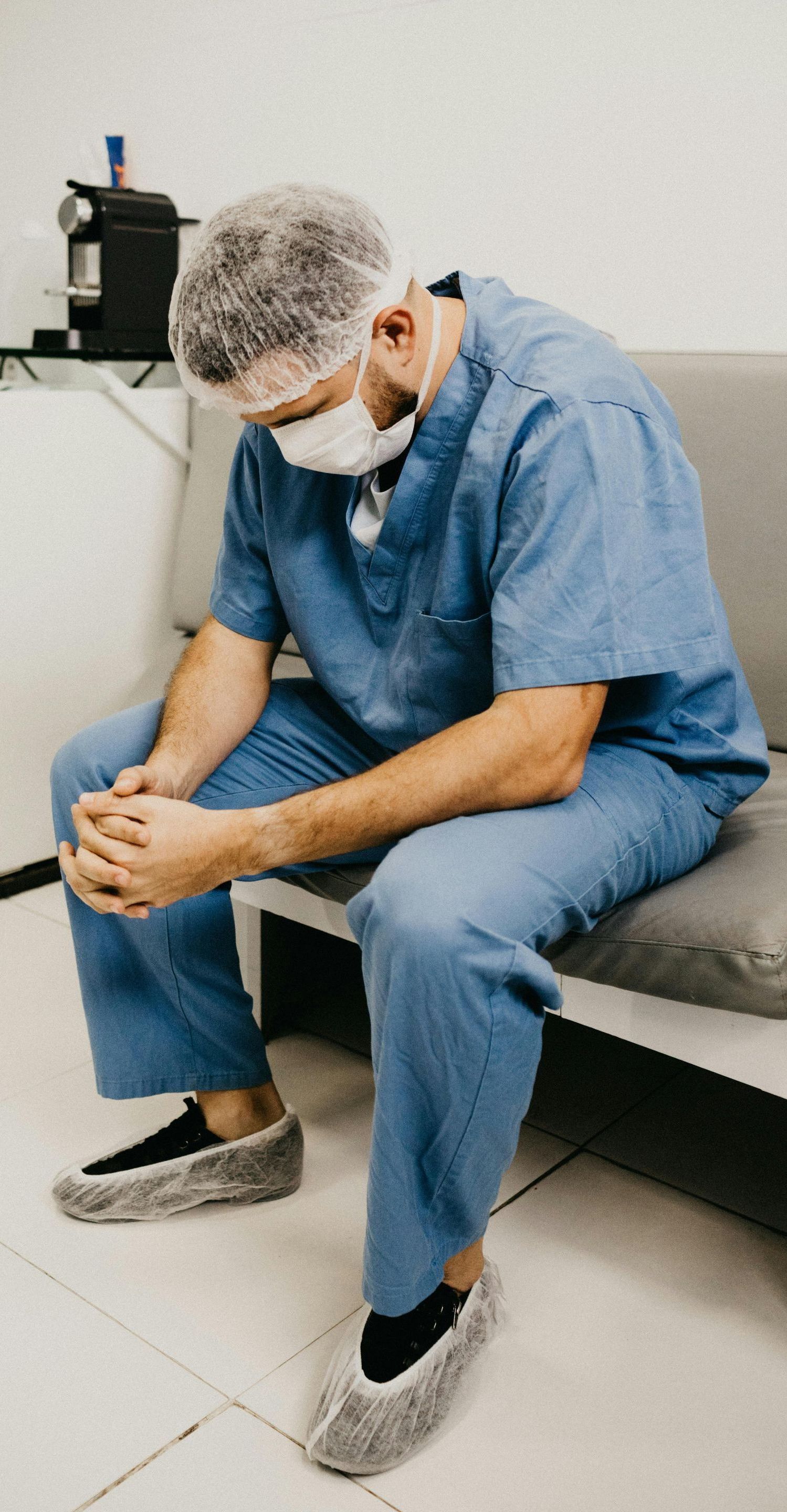A surgeon is sitting on a couch with his head down.