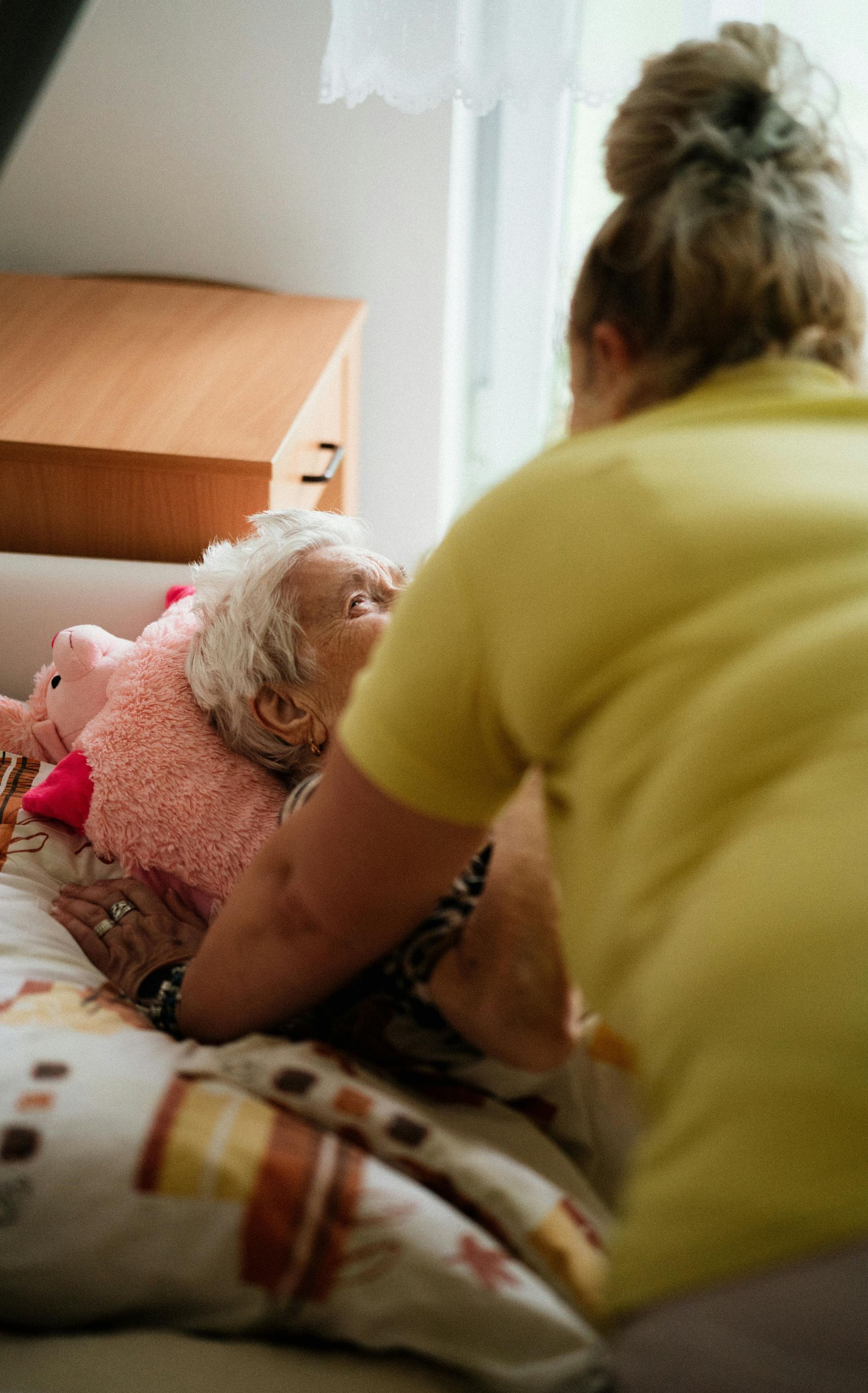 an elderly woman is laying on a bed with a stuffed animal .