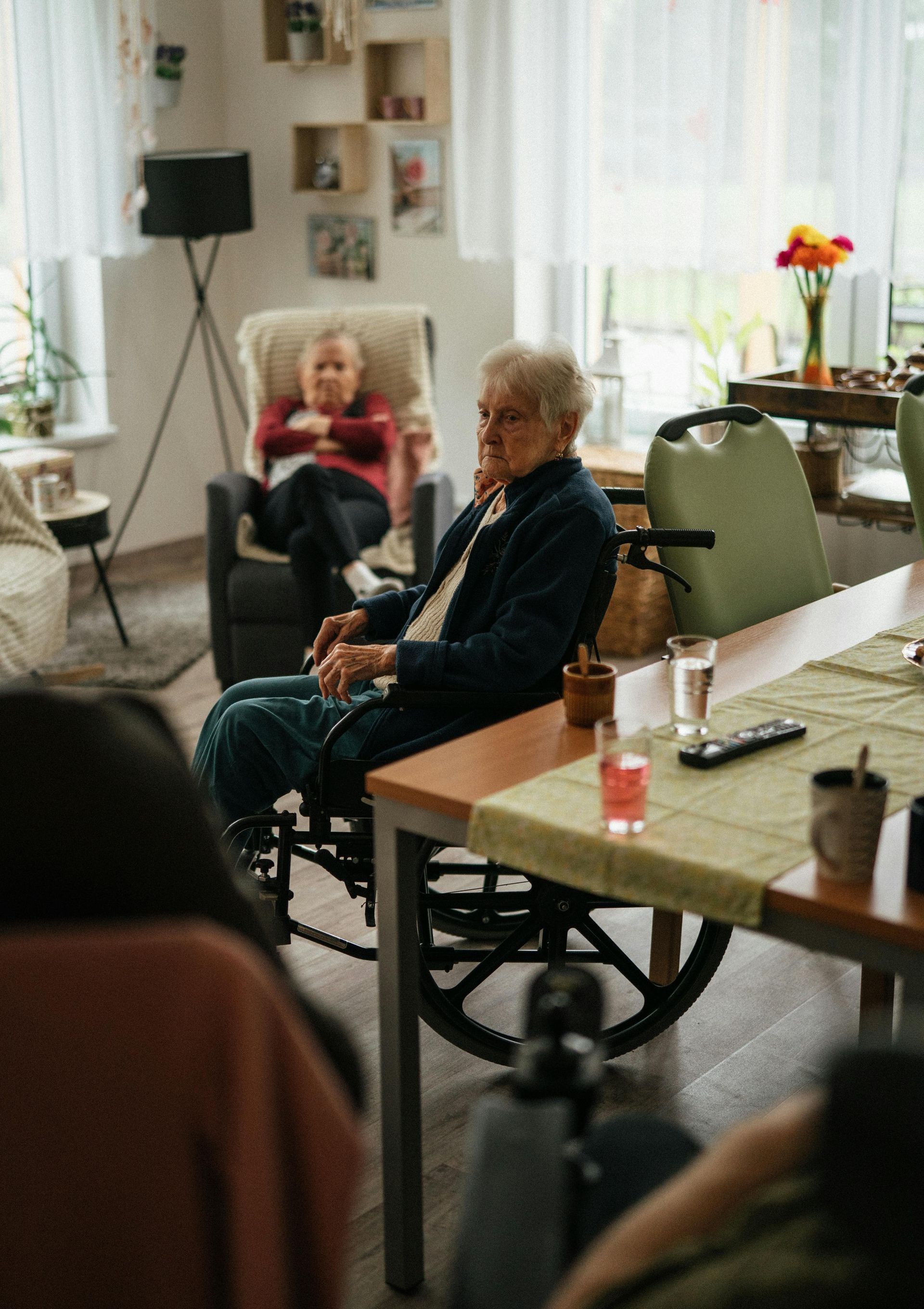 An elderly man in a wheelchair is sitting at a table in a living room.