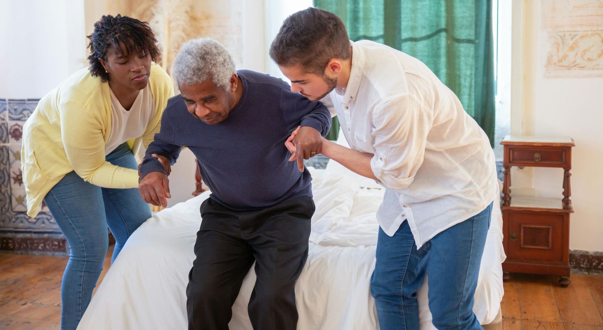 two people helping elderly man into bed