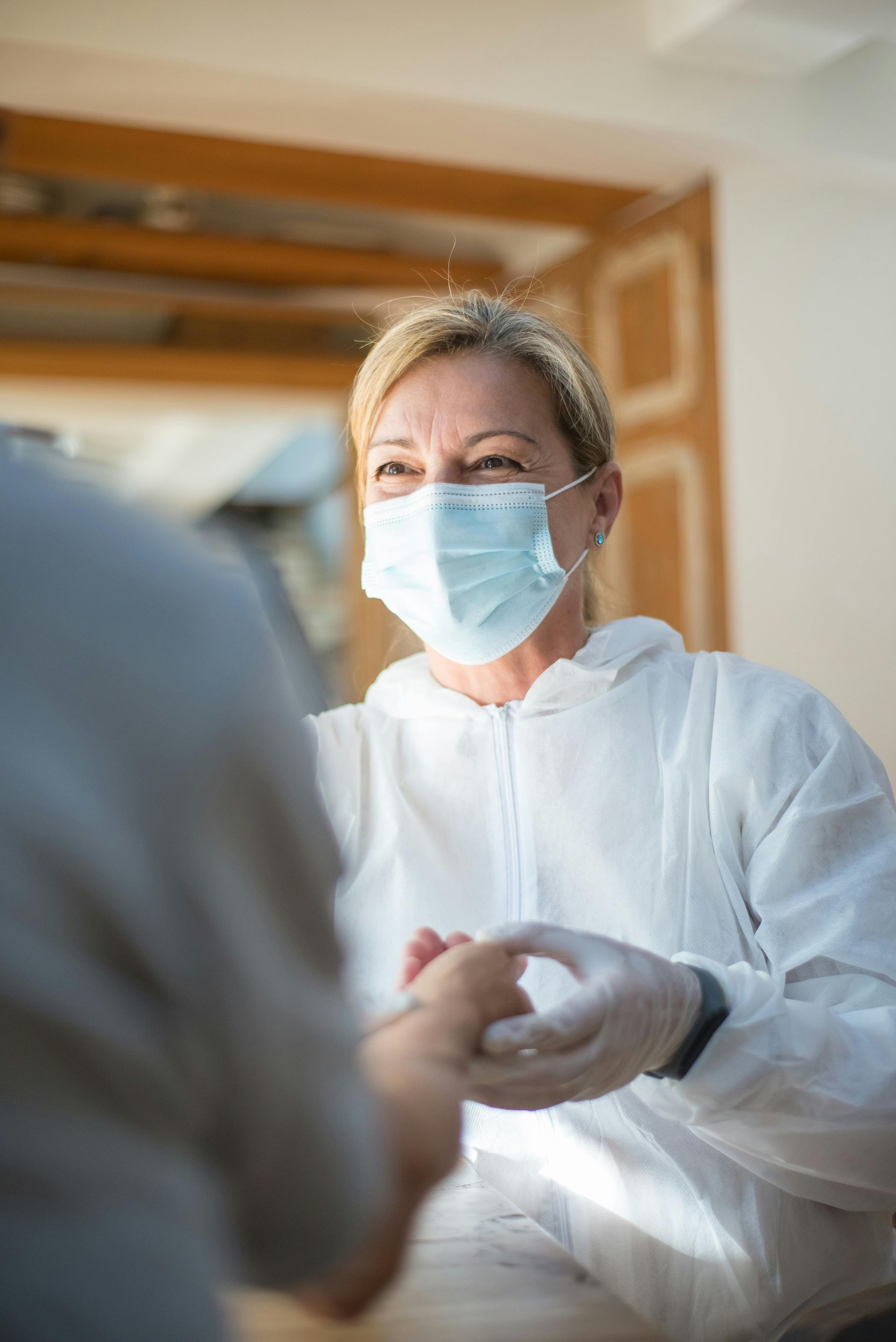 a nurse wearing a mask and gloves is holding a patient 's hand 