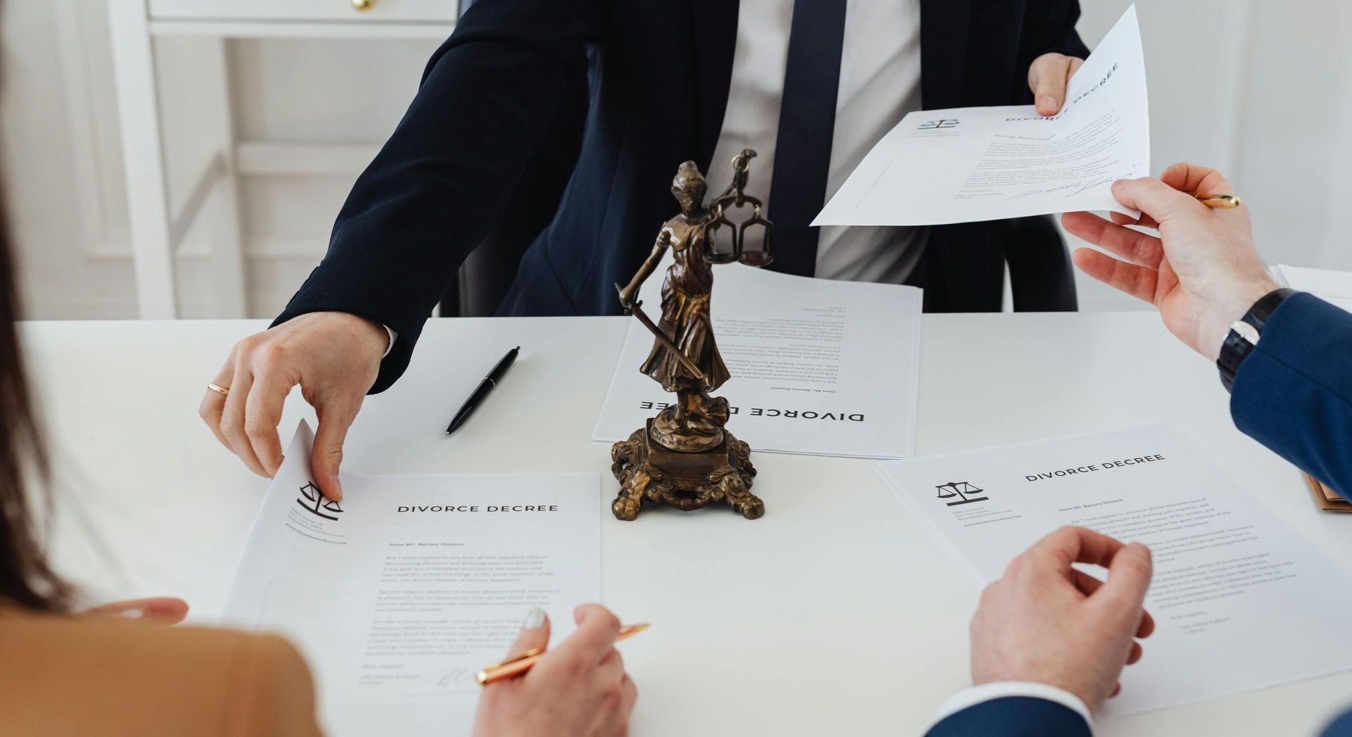 A group of people are sitting at a table with papers and a statue of justice.
