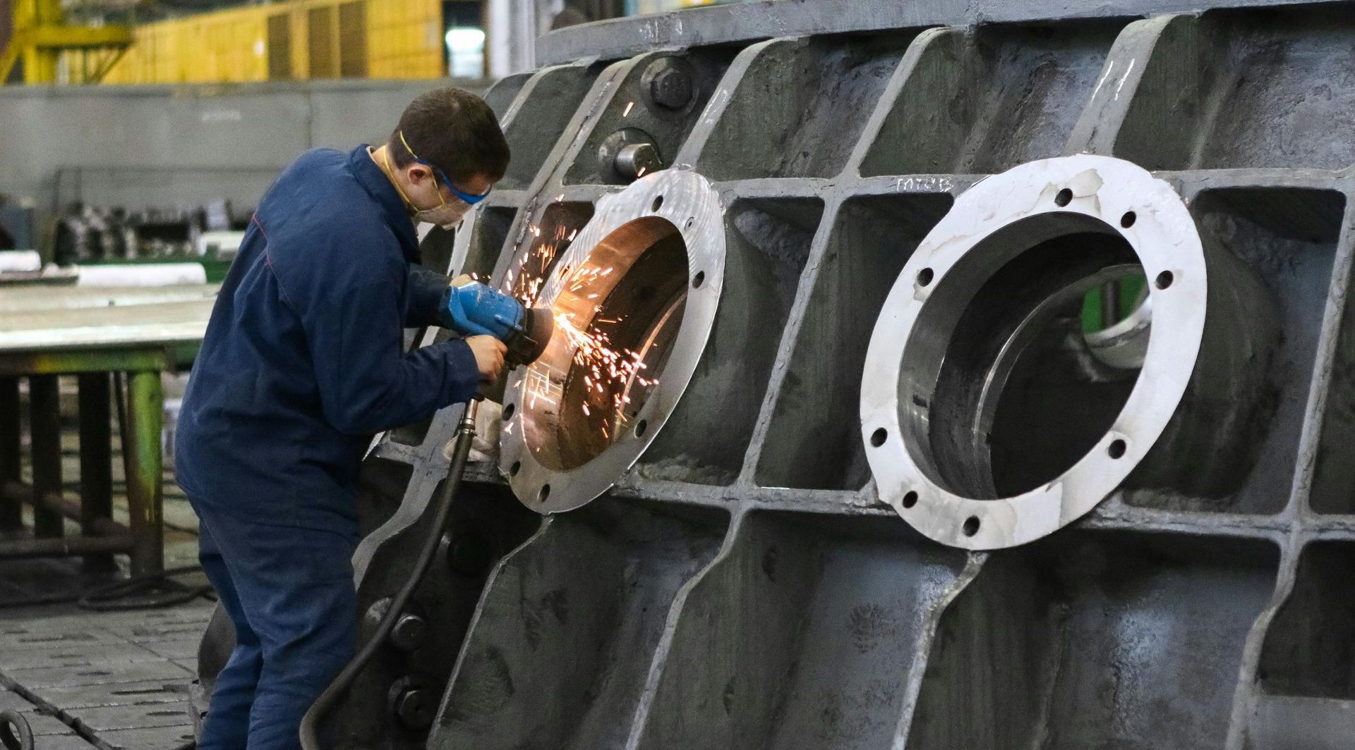A man is grinding a piece of metal in a factory.