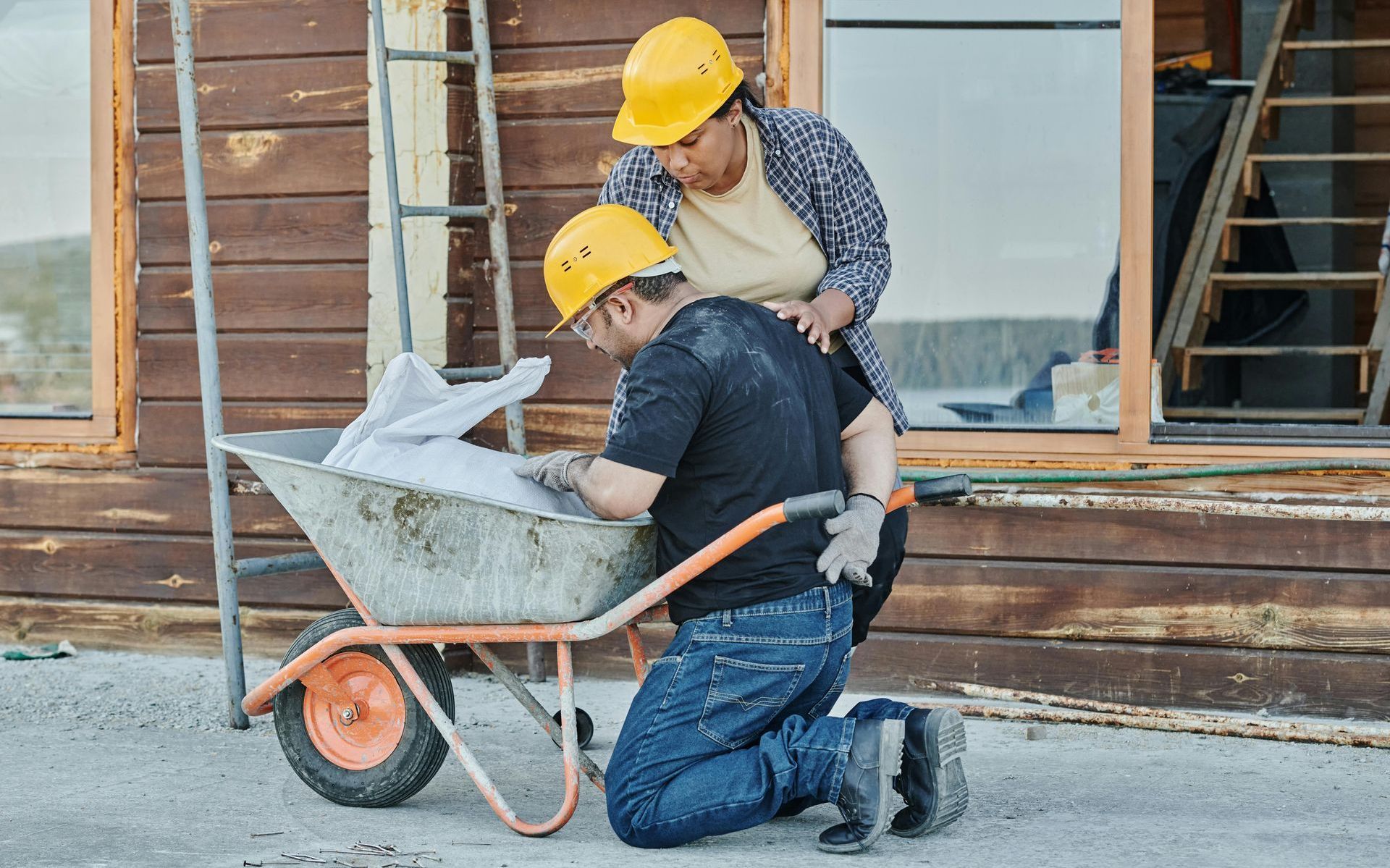A man and a woman are kneeling next to a wheelbarrow.
