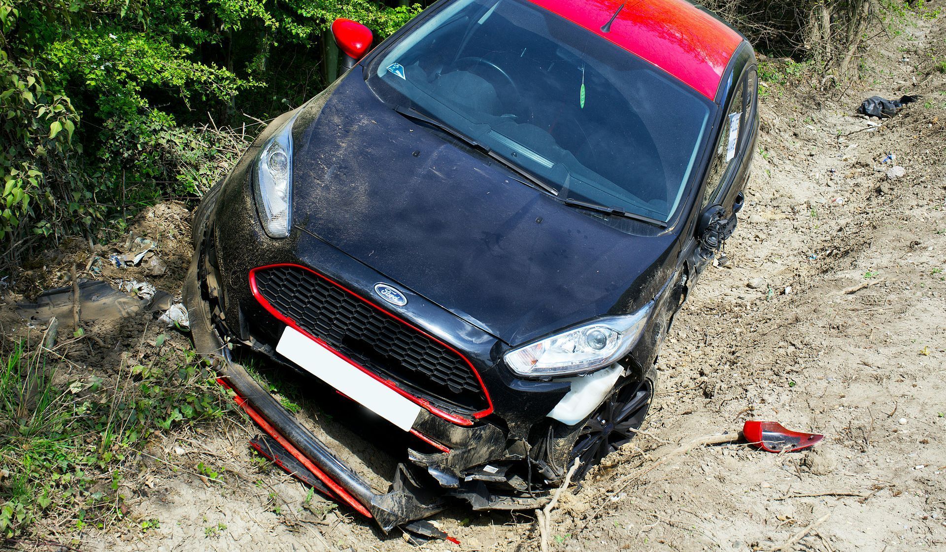 A black car is laying on its side in the dirt.