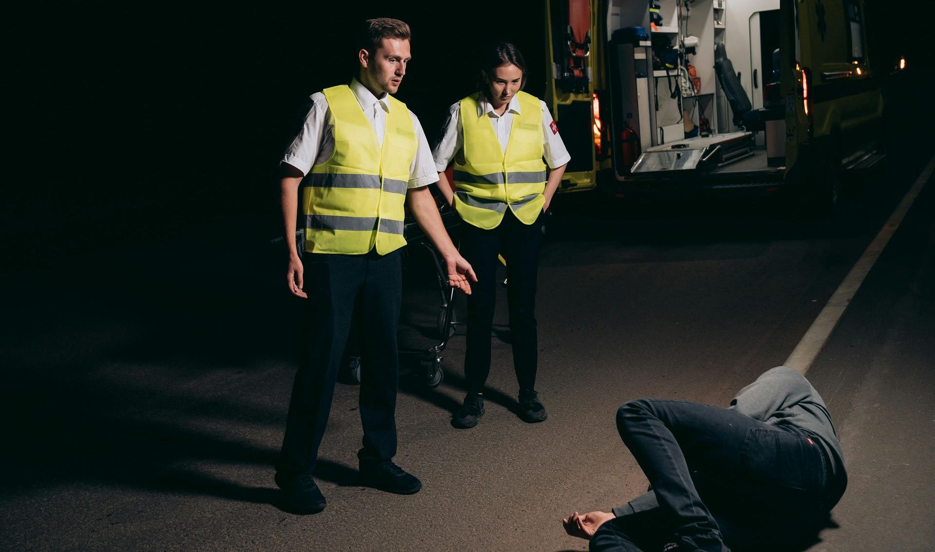 Two paramedics are standing next to a man laying on the ground.