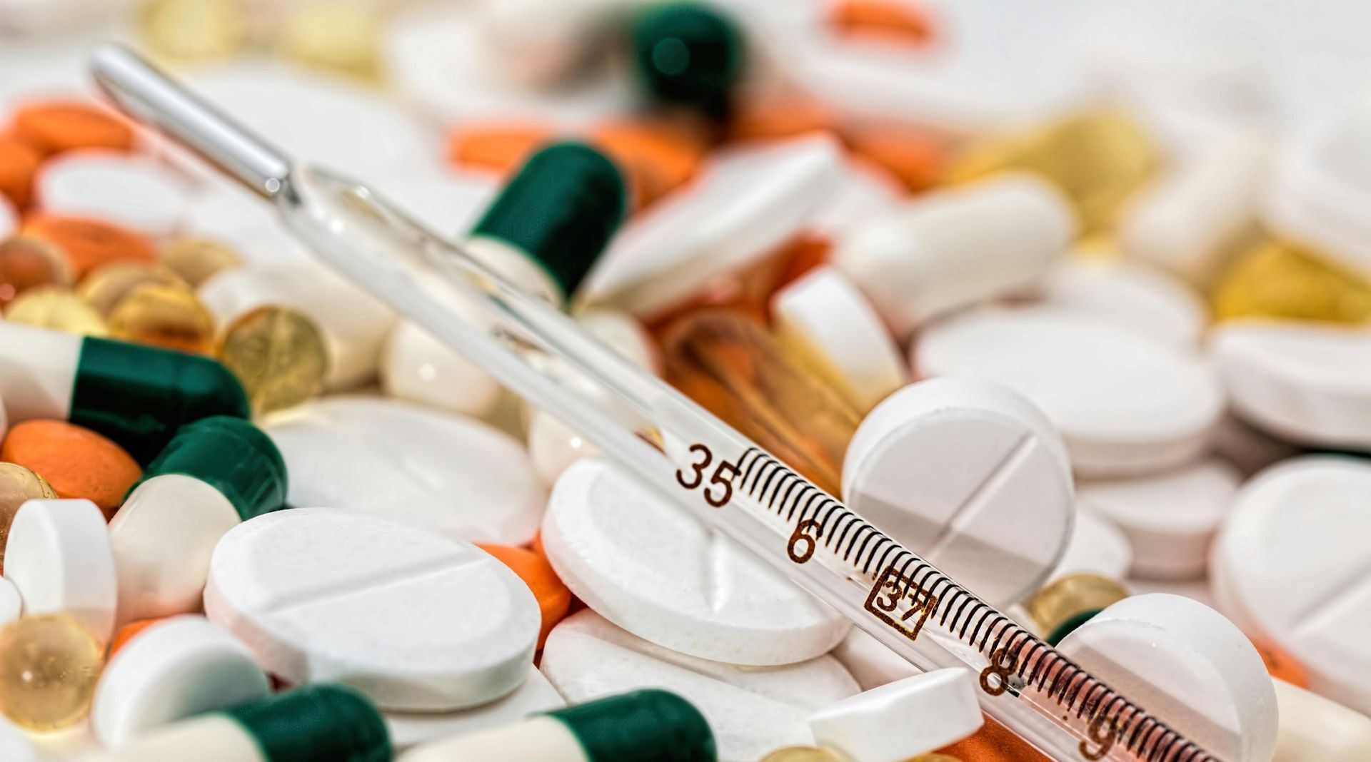 A thermometer is sitting on top of a pile of pills and capsules.