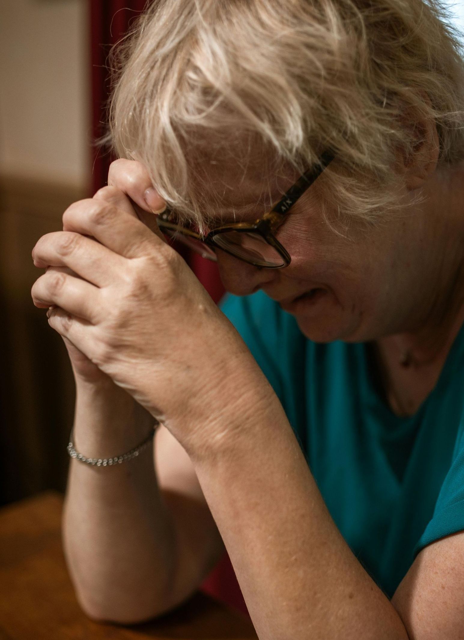 A woman is sitting at a table with her hands folded in prayer.